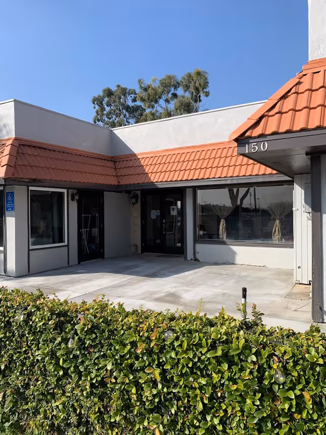 Exterior view of a senior living facility front entrance with red-tiled awning and hedges.