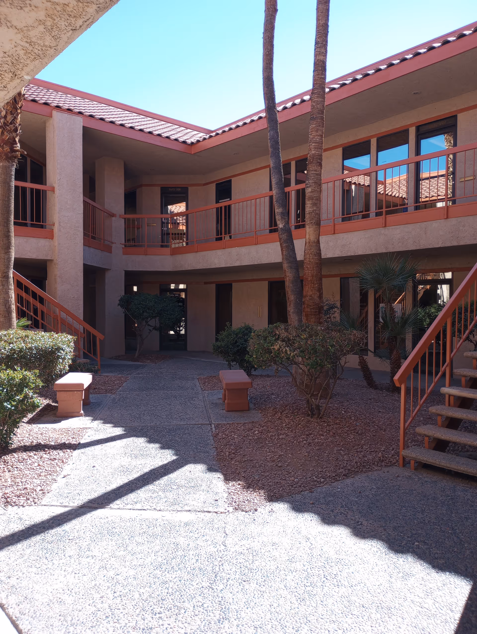 Two-story beige senior living building courtyard with palm trees, stairs, and benches.