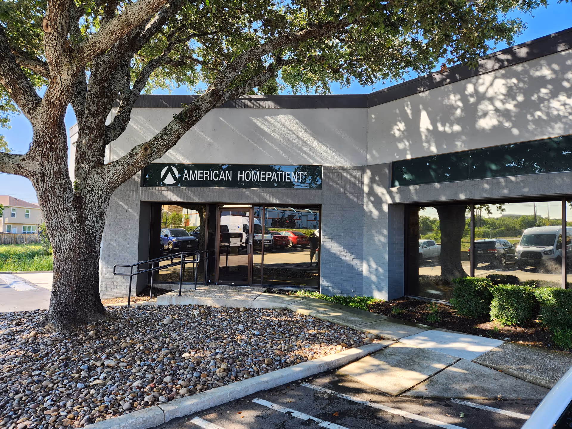 Exterior view of American HomePatient facility entrance with glass doors and a large tree.