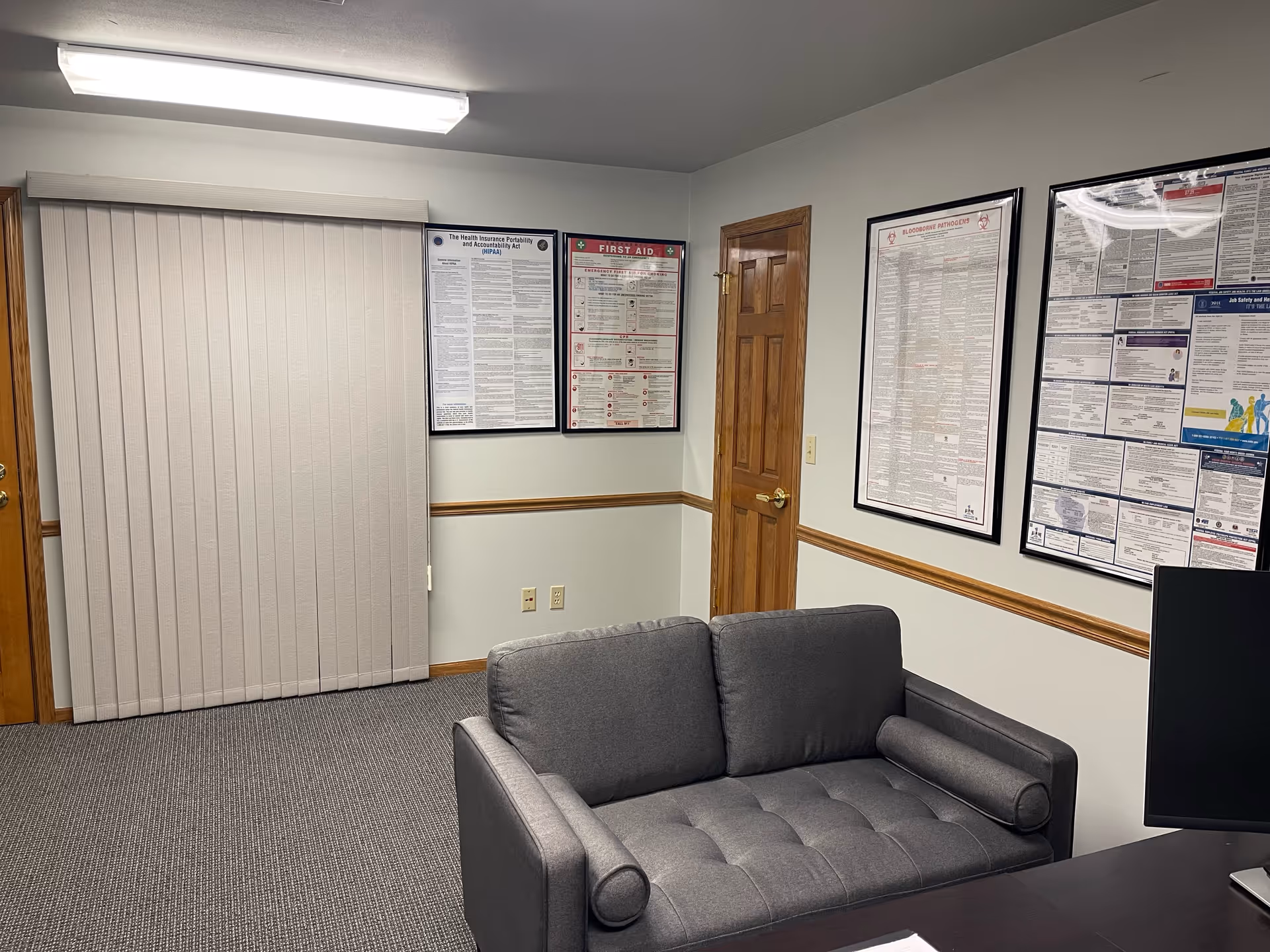 Gray sofa faces framed posters and a desk in a small office-like waiting area.