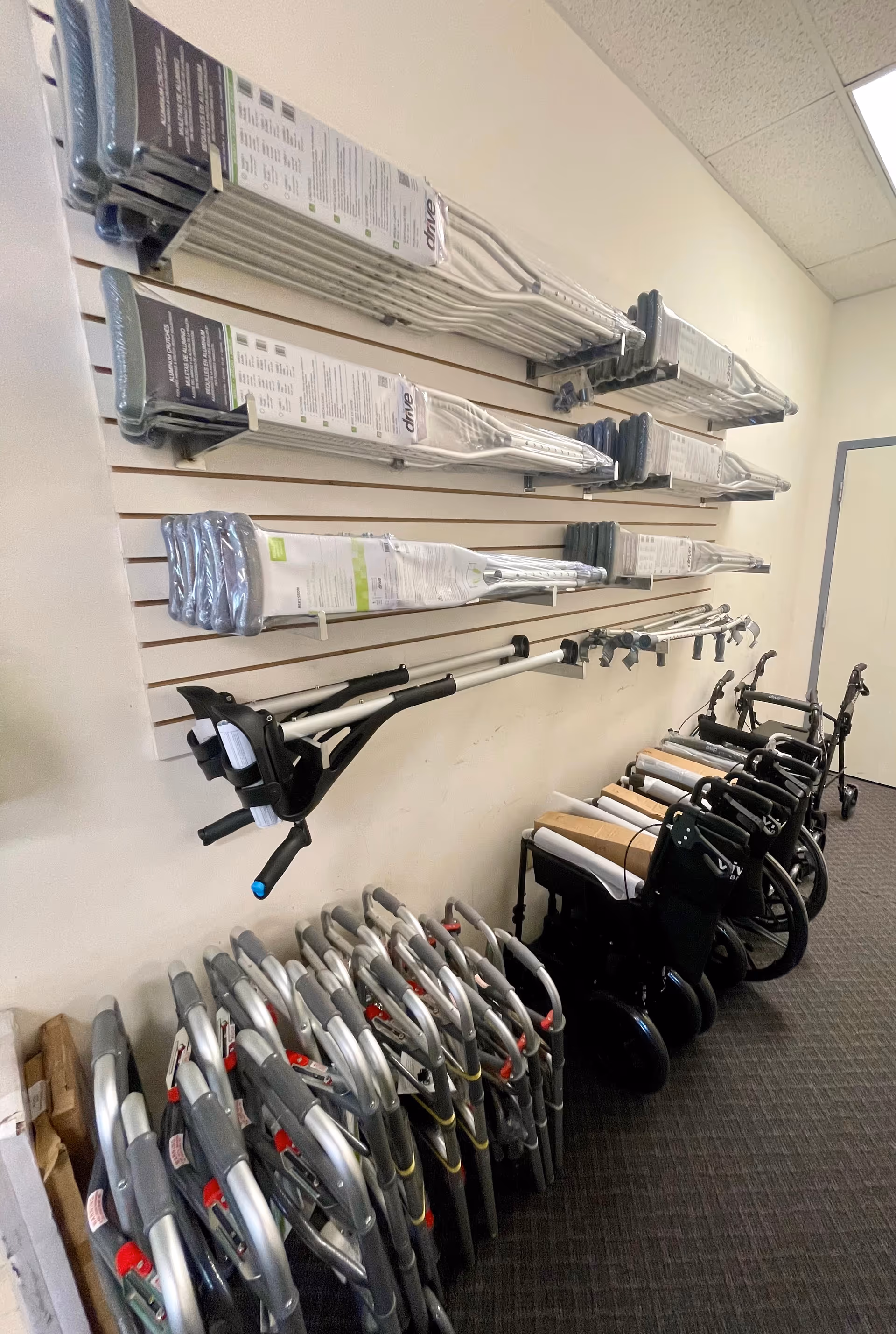 Interior storage area with wall racks of folded mobility aids and lined-up wheelchairs.