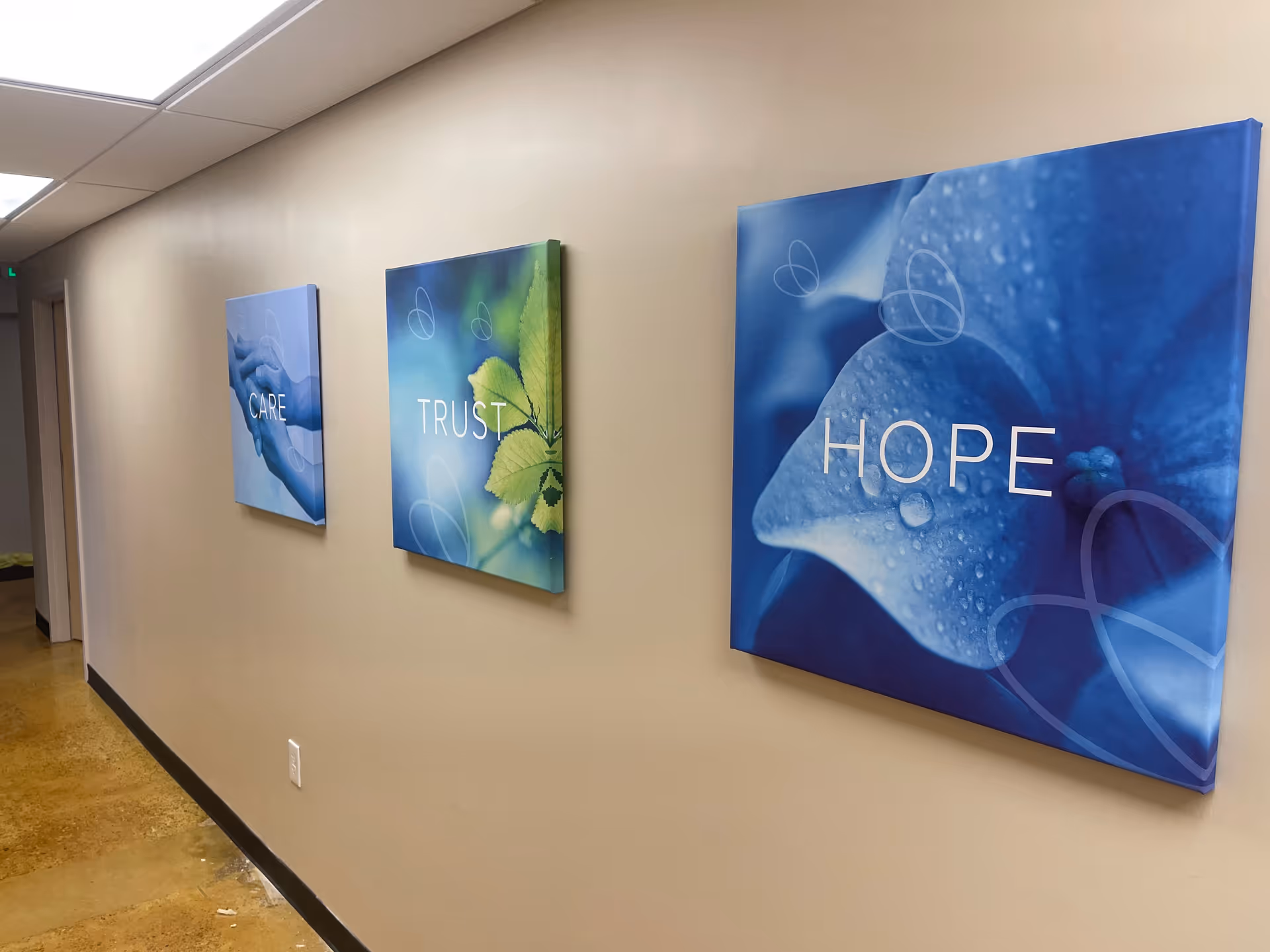 Interior hallway with three wall-mounted blue inspirational canvases reading CARE, TRUST, and HOPE.