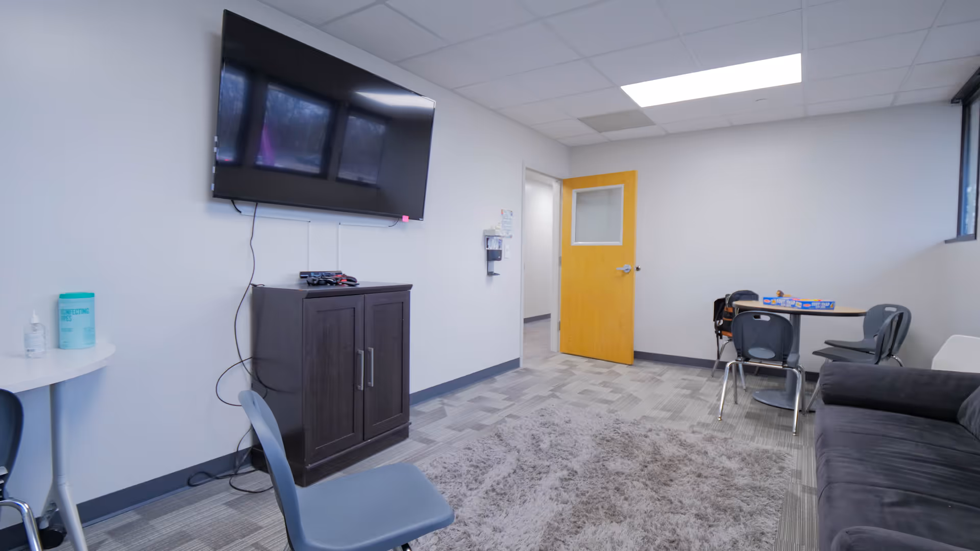 Lounge area in a senior facility with wall-mounted TV, cabinet, sofa, and seating.