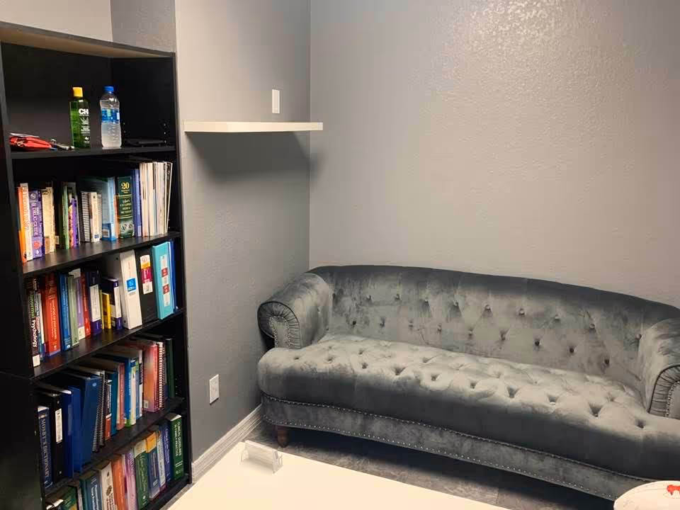 Grey tufted sofa beside tall bookshelf filled with books in a small lounge