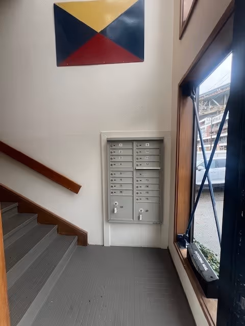 Interior stairwell with wall-mounted mailboxes beside a window and geometric wall art.