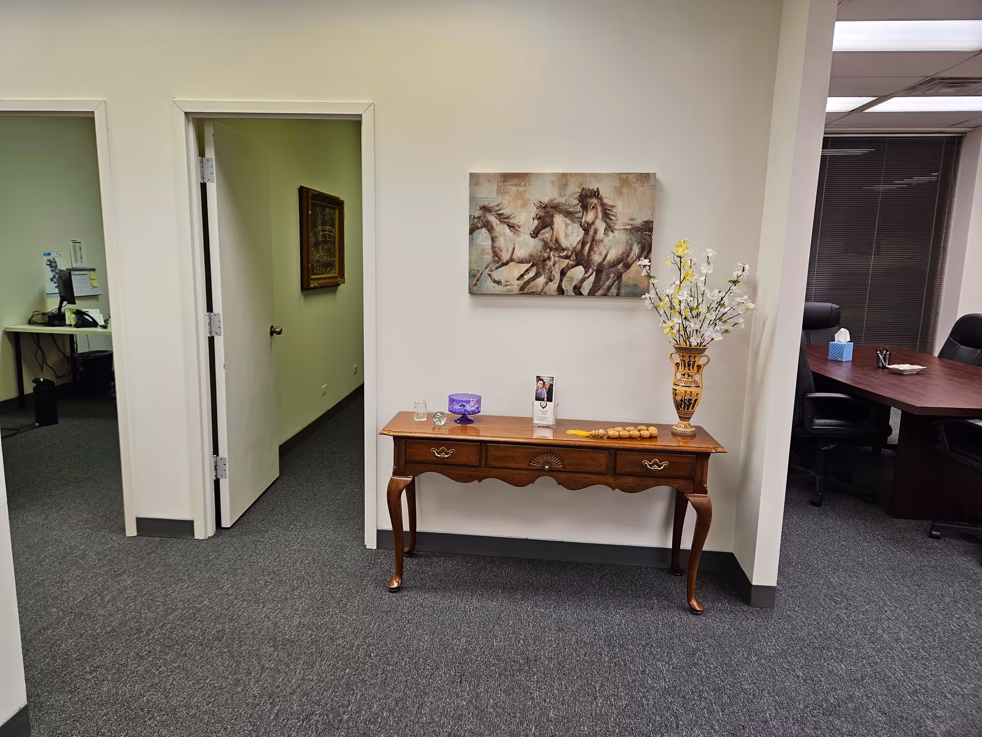 Wooden console table with decorative items in a hallway, horse painting on wall.