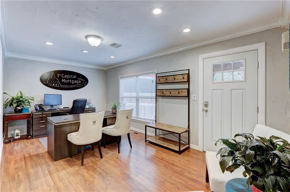 Office reception area with desk, two cream chairs, wall sign, window, and plants.