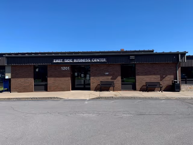 Exterior view of a brick building labeled East Side Business Center with glass doors and benches