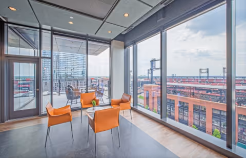 Bright interior lounge with orange chairs and glass walls overlooking a cityscape.