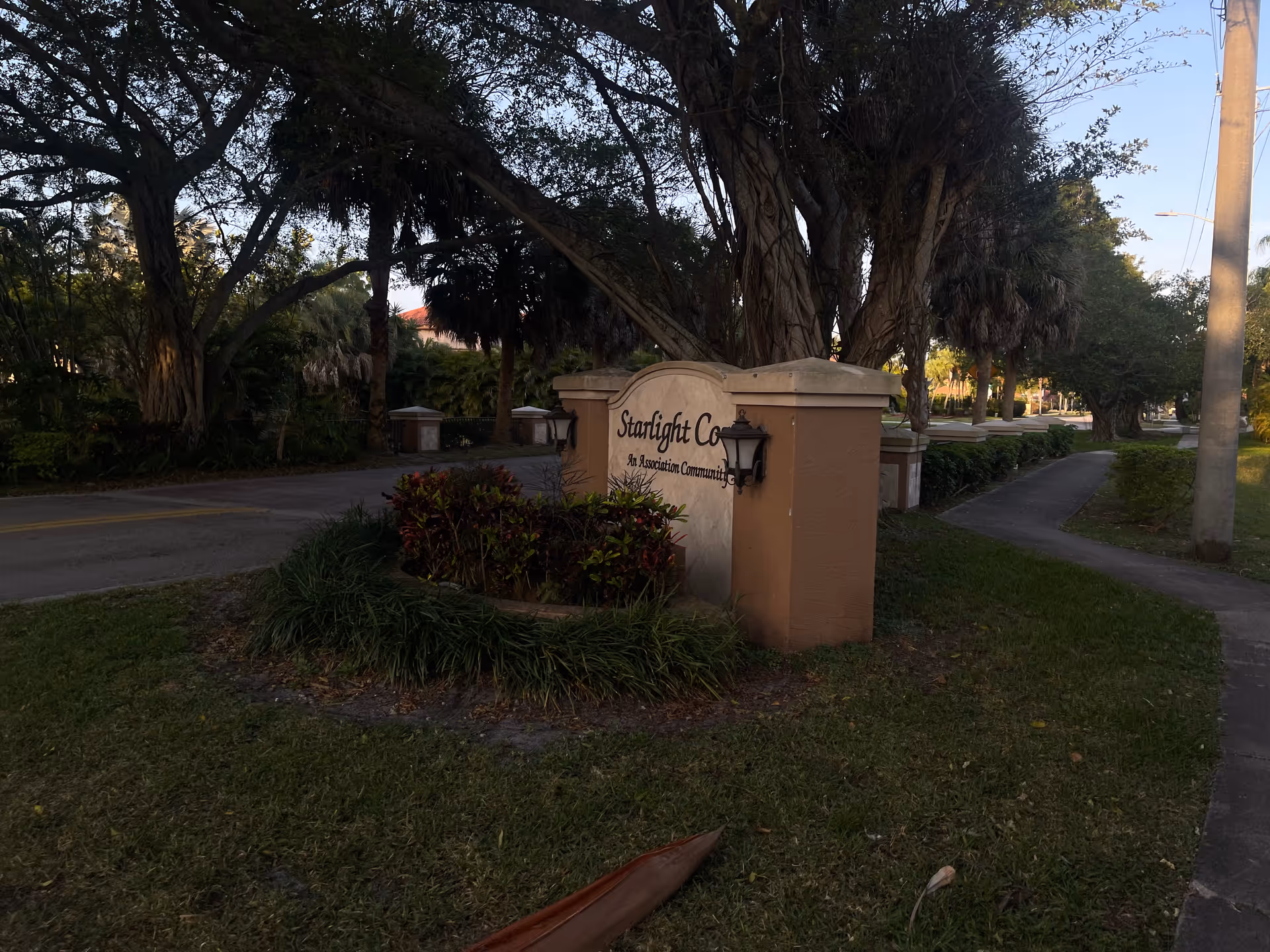 Entrance sign with landscaping and a tree-lined street, marking a community entrance.
