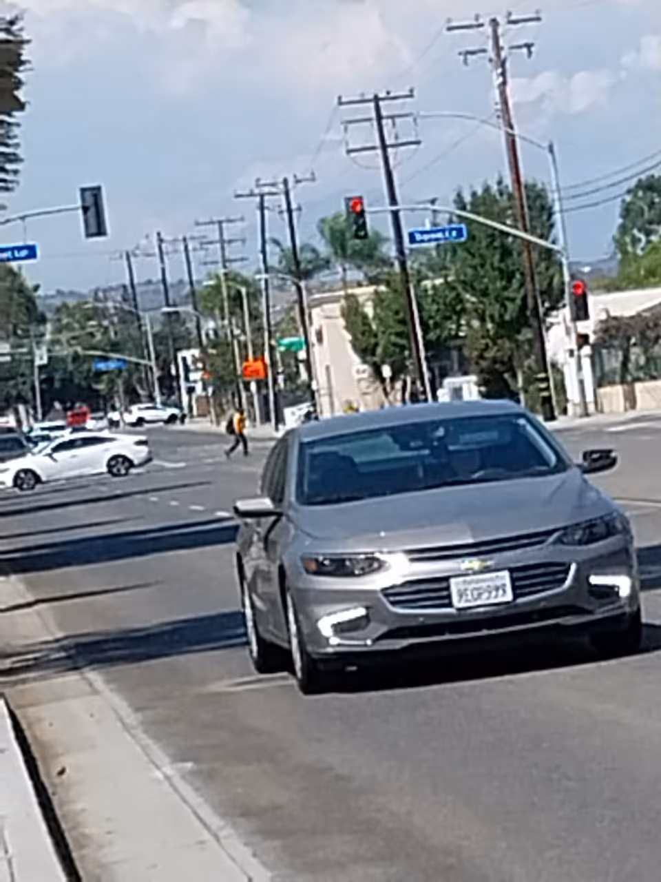 Silver sedan on a sunlit urban street with traffic signals and utility poles.