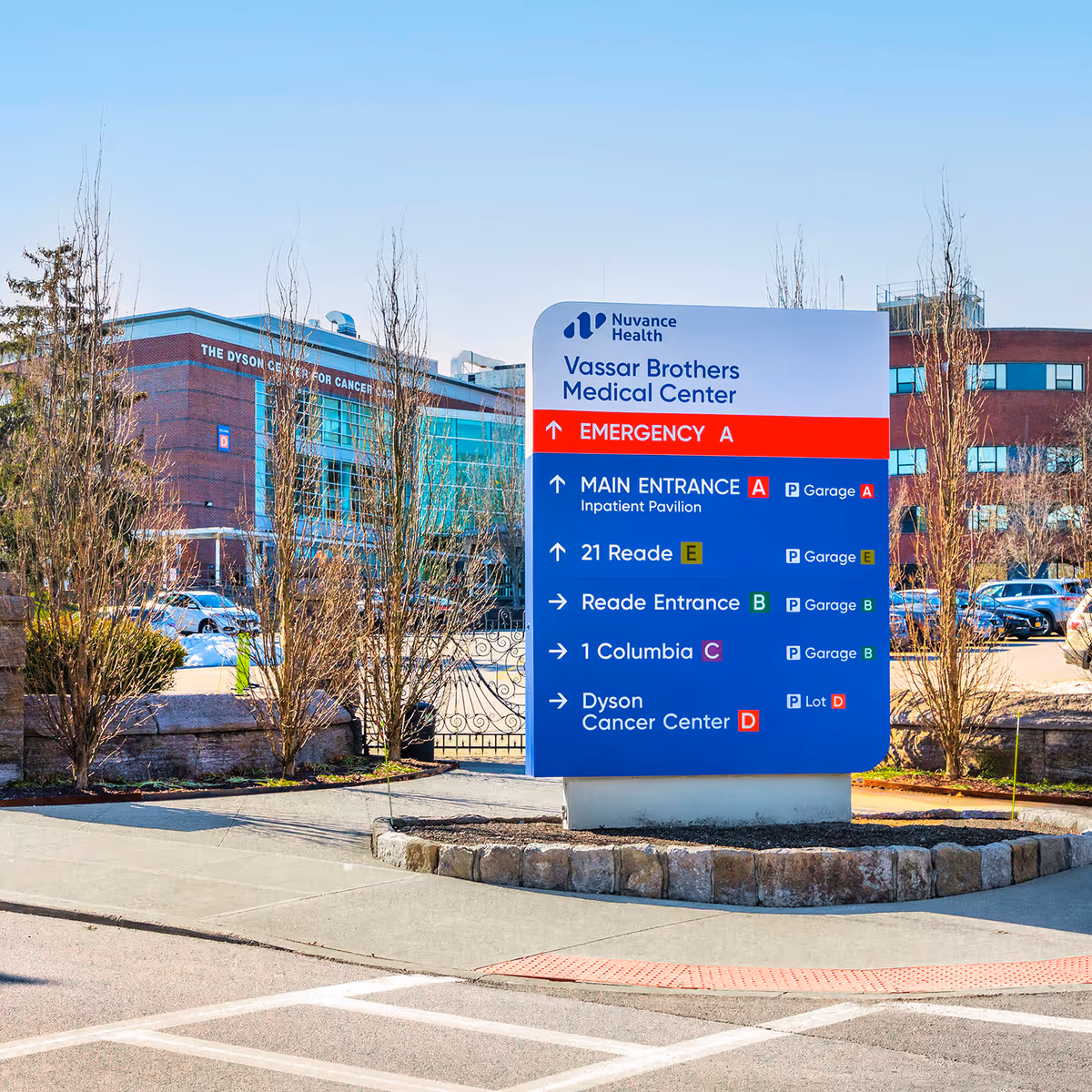 Large outdoor directional sign for a medical campus stands in a parking lot near buildings.