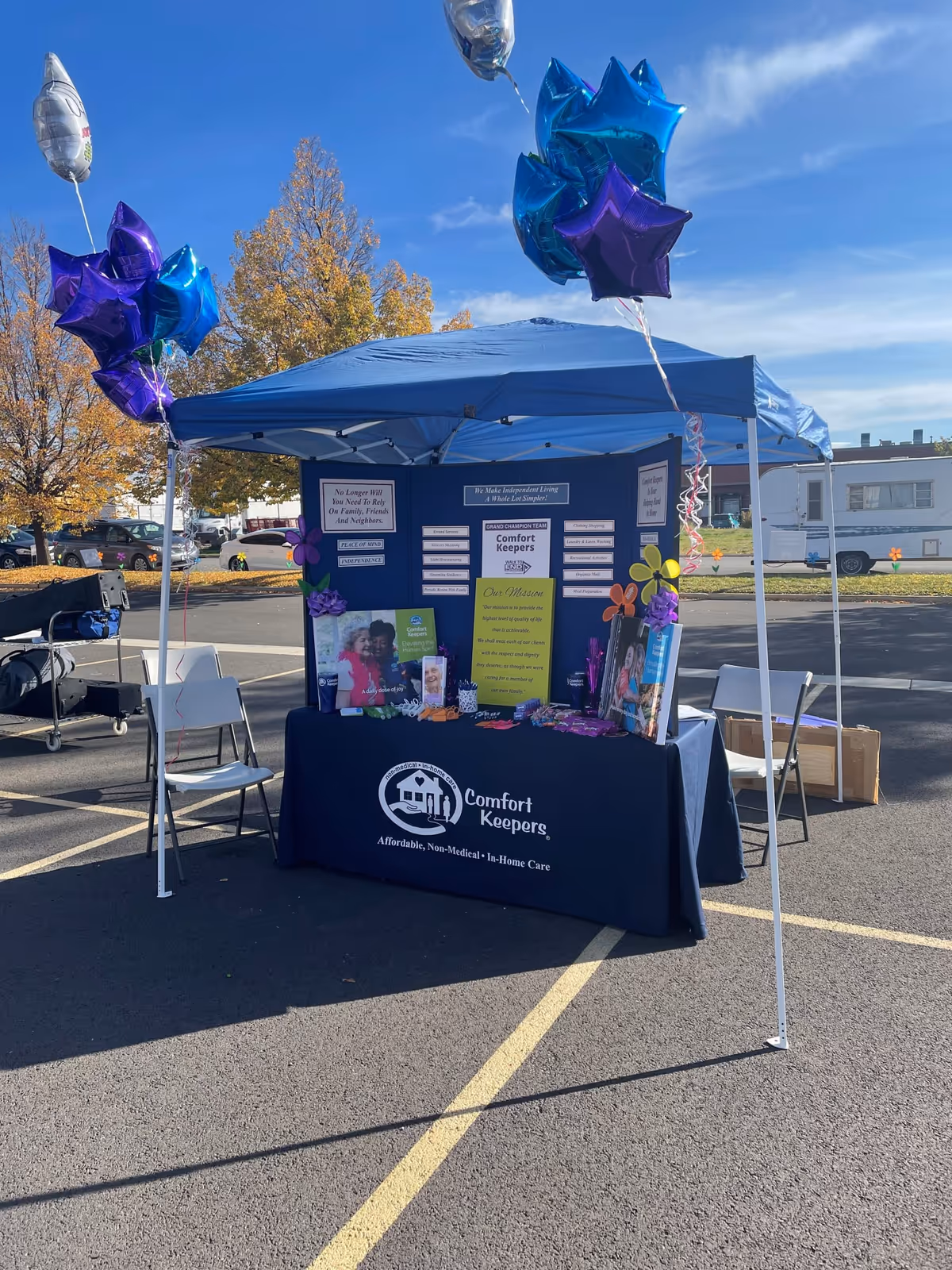 Blue canopy booth for Comfort Keepers with balloons and brochures in a parking lot.
