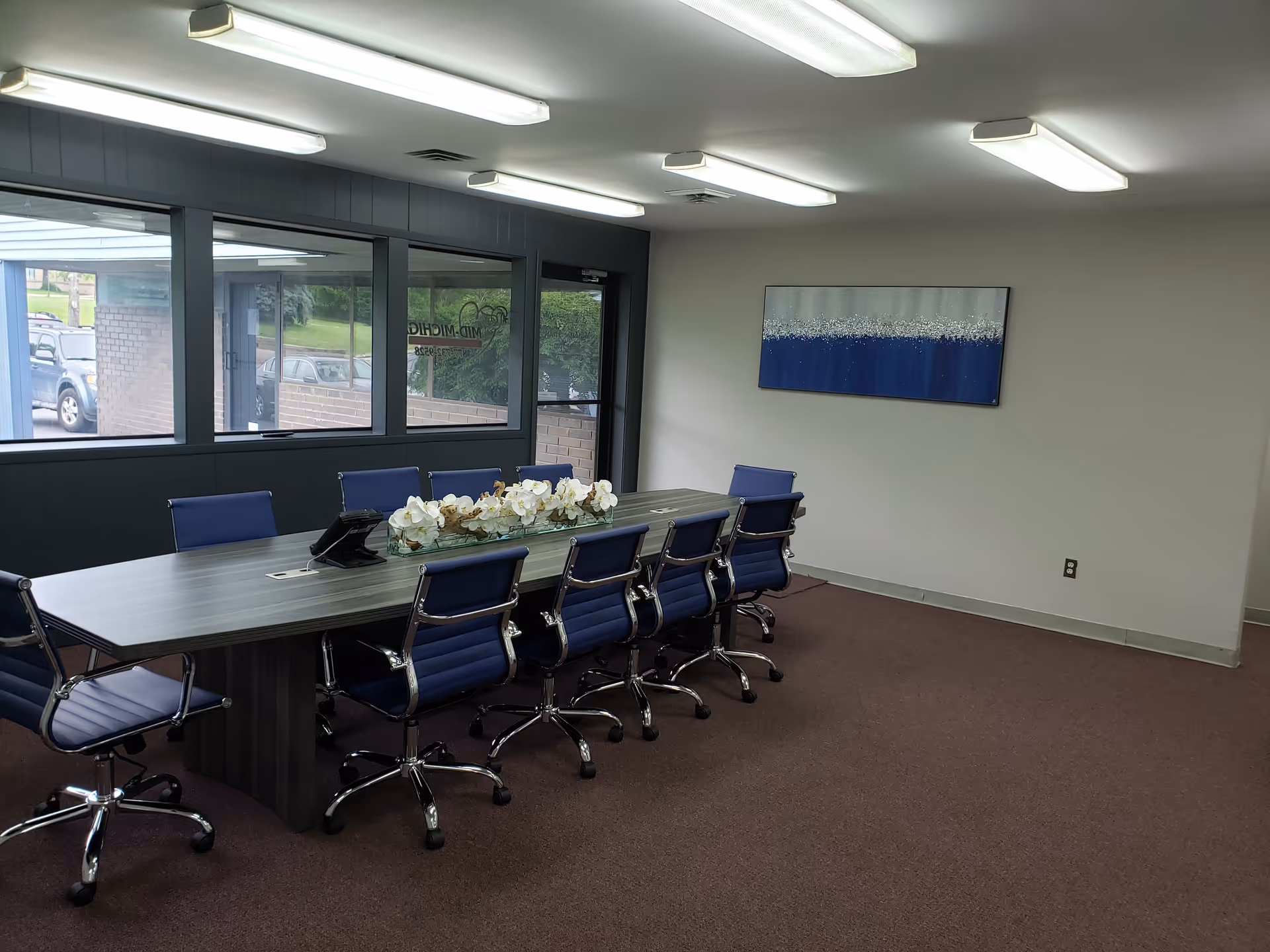 Interior conference room with a long table, blue chairs, and a white flower centerpiece.