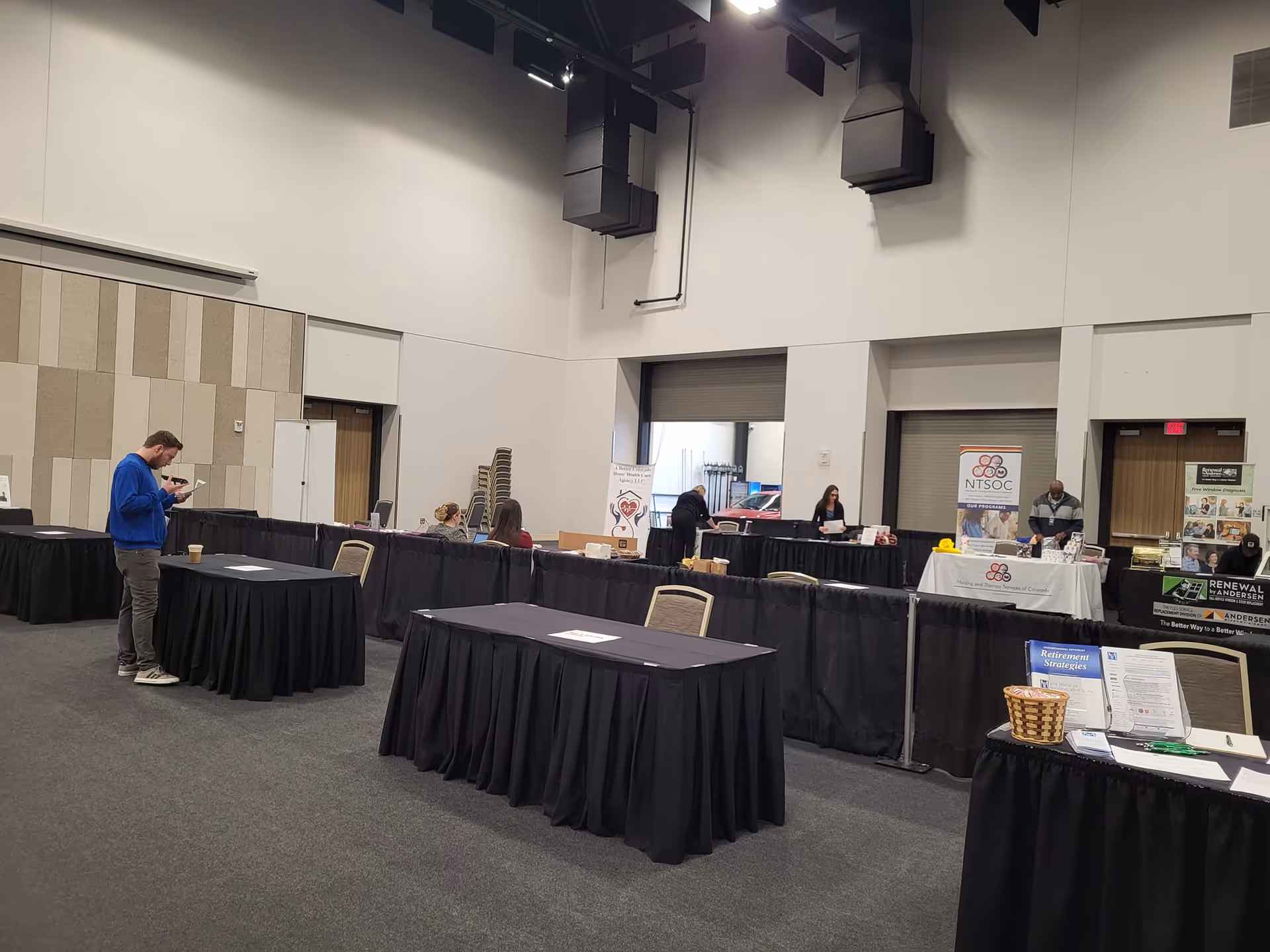 Large indoor expo hall with black-draped vendor tables and a few attendees walking.