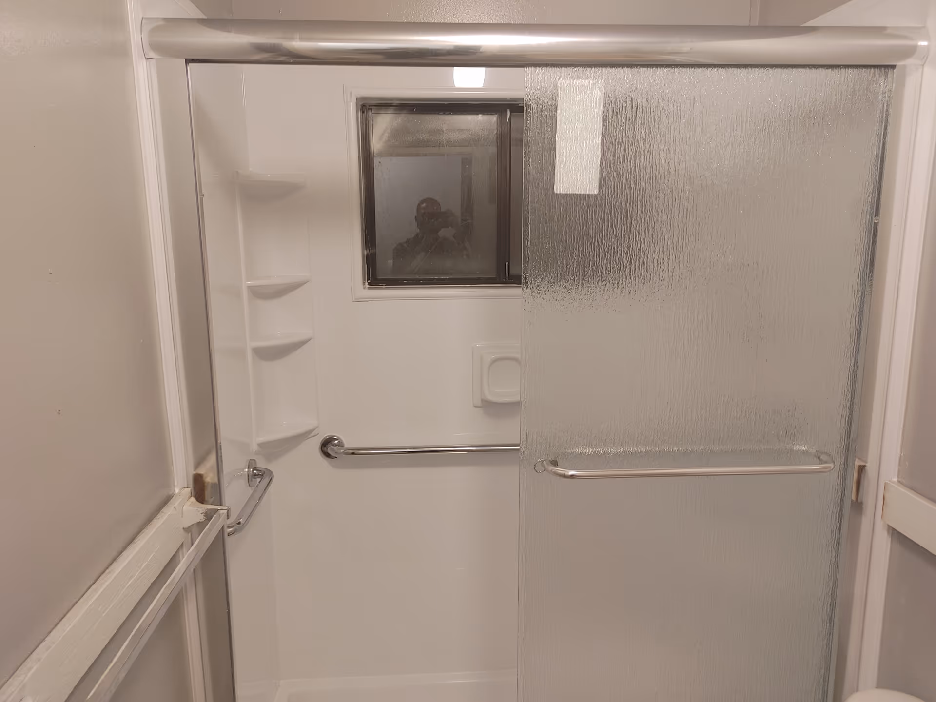 An enclosed shower area with a sliding frosted door, built-in shelves, and grab bars.