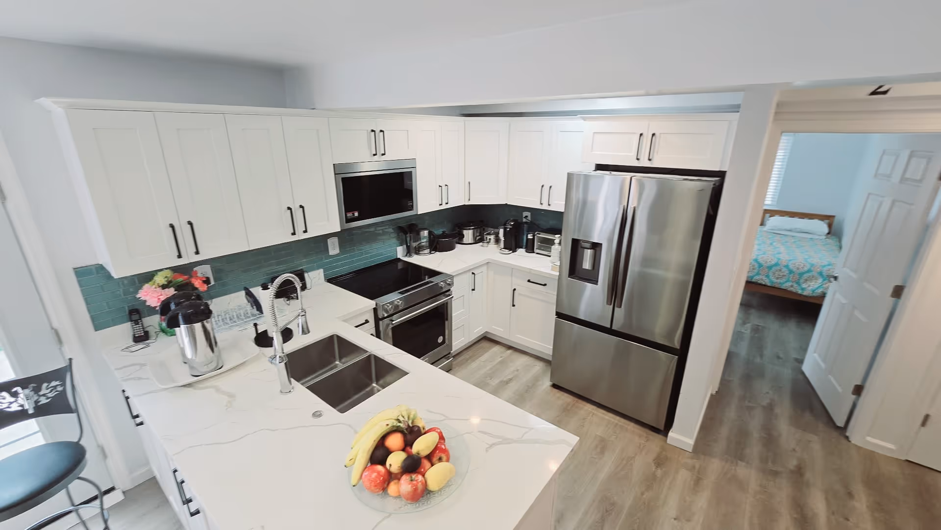 Bright white kitchen with stainless steel appliances, island, and fruit bowl.