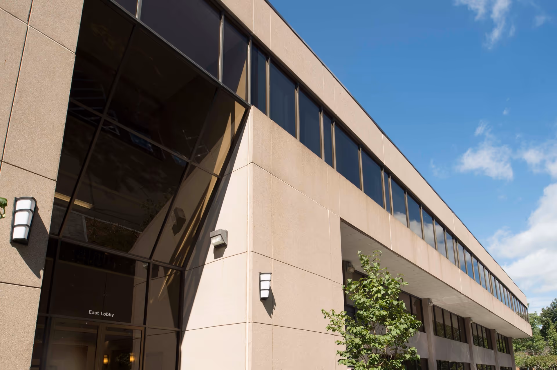 Exterior view of a beige modern building with large glass windows and blue sky.
