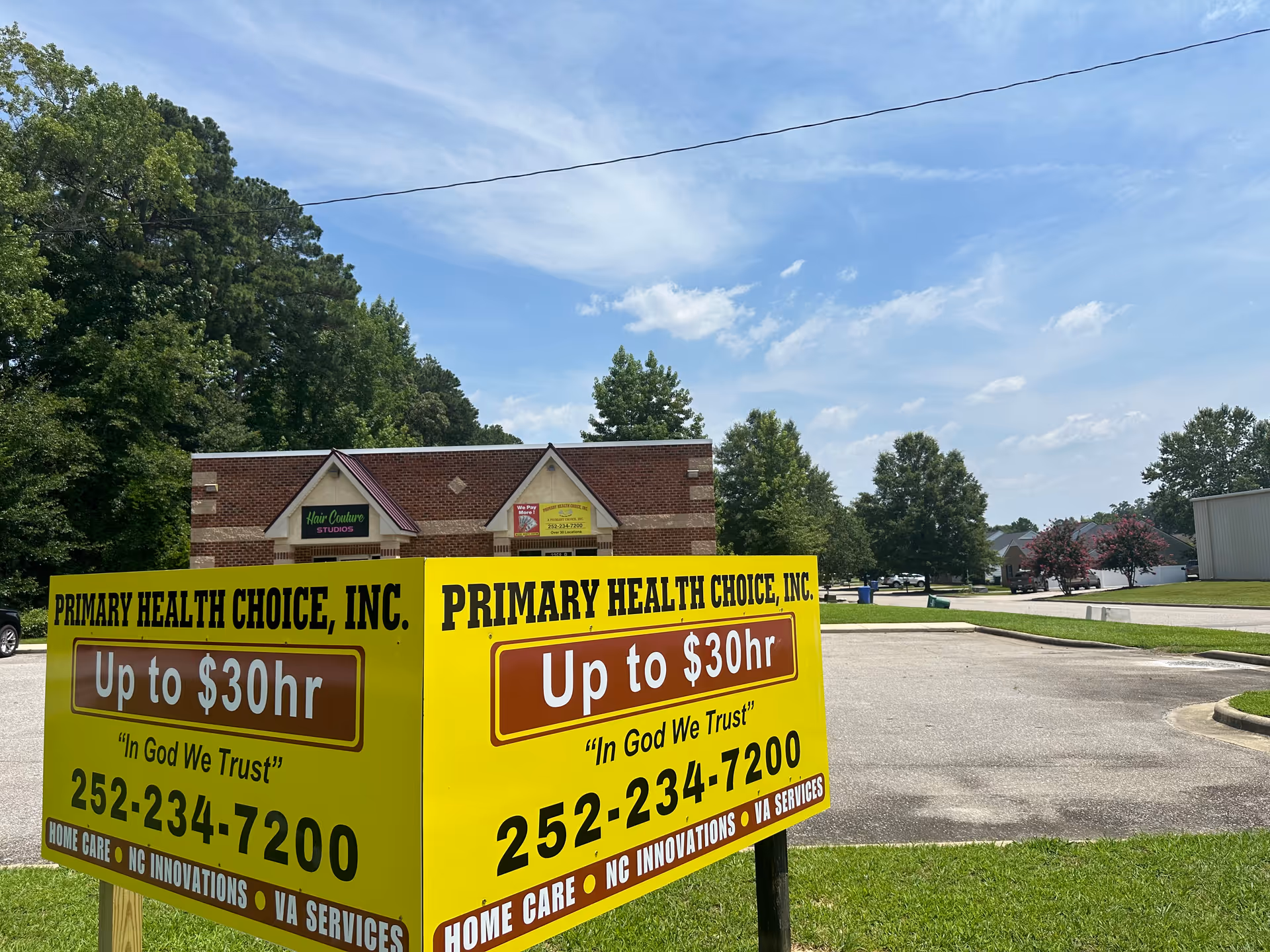 Bright yellow Primary Health Choice signs advertise services in a parking lot with a brick building.