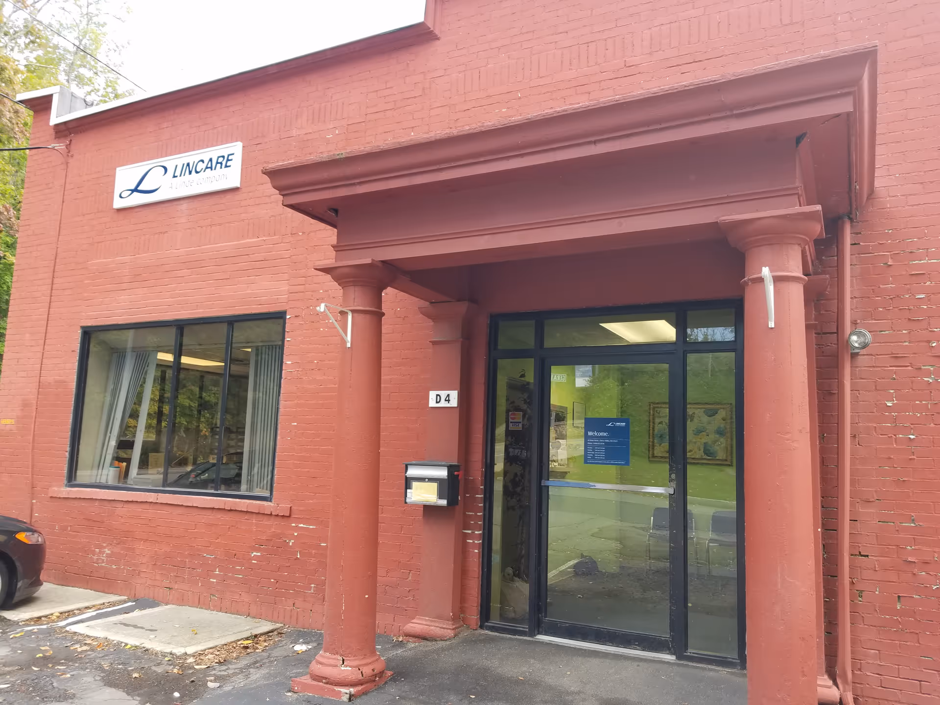 Front entrance of a red brick LINCARE facility with large glass doors and columns.