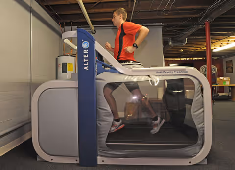 Person runs on an AlterG anti-gravity treadmill inside a therapy facility gym.