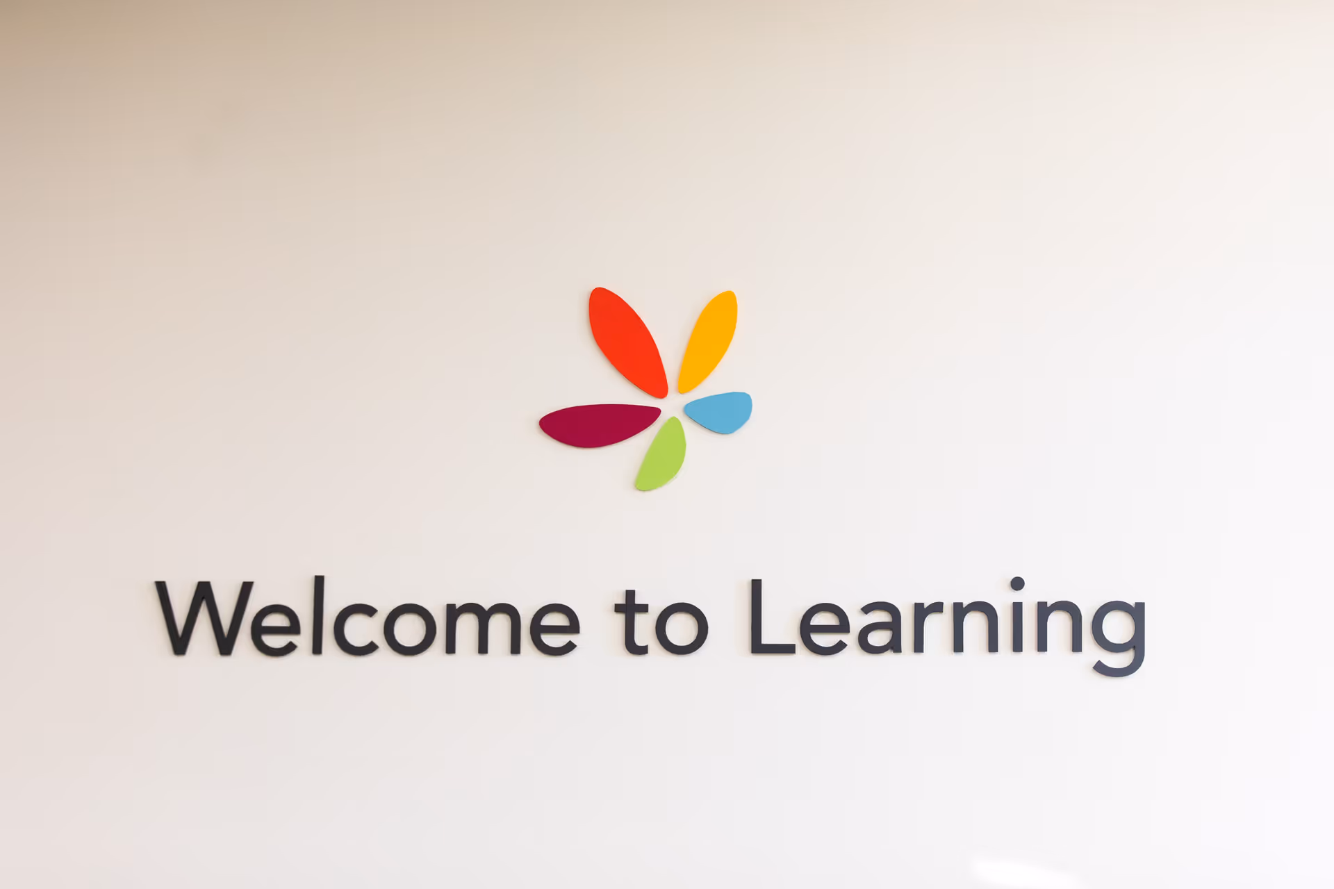White wall features a colorful flower logo above the 'Welcome to Learning' sign.