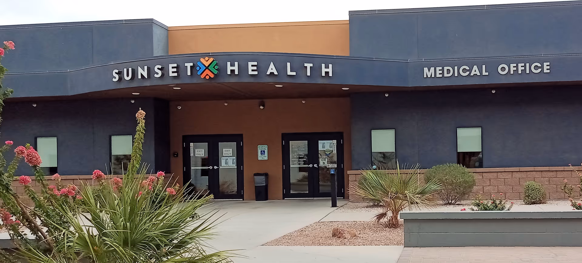 Front view of Sunset Health Medical Office, blue exterior, glass entry doors, desert landscaping.
