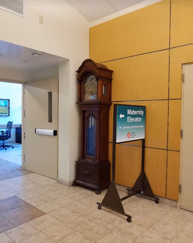 Hallway interior with an antique grandfather clock beside a maternity elevator sign.