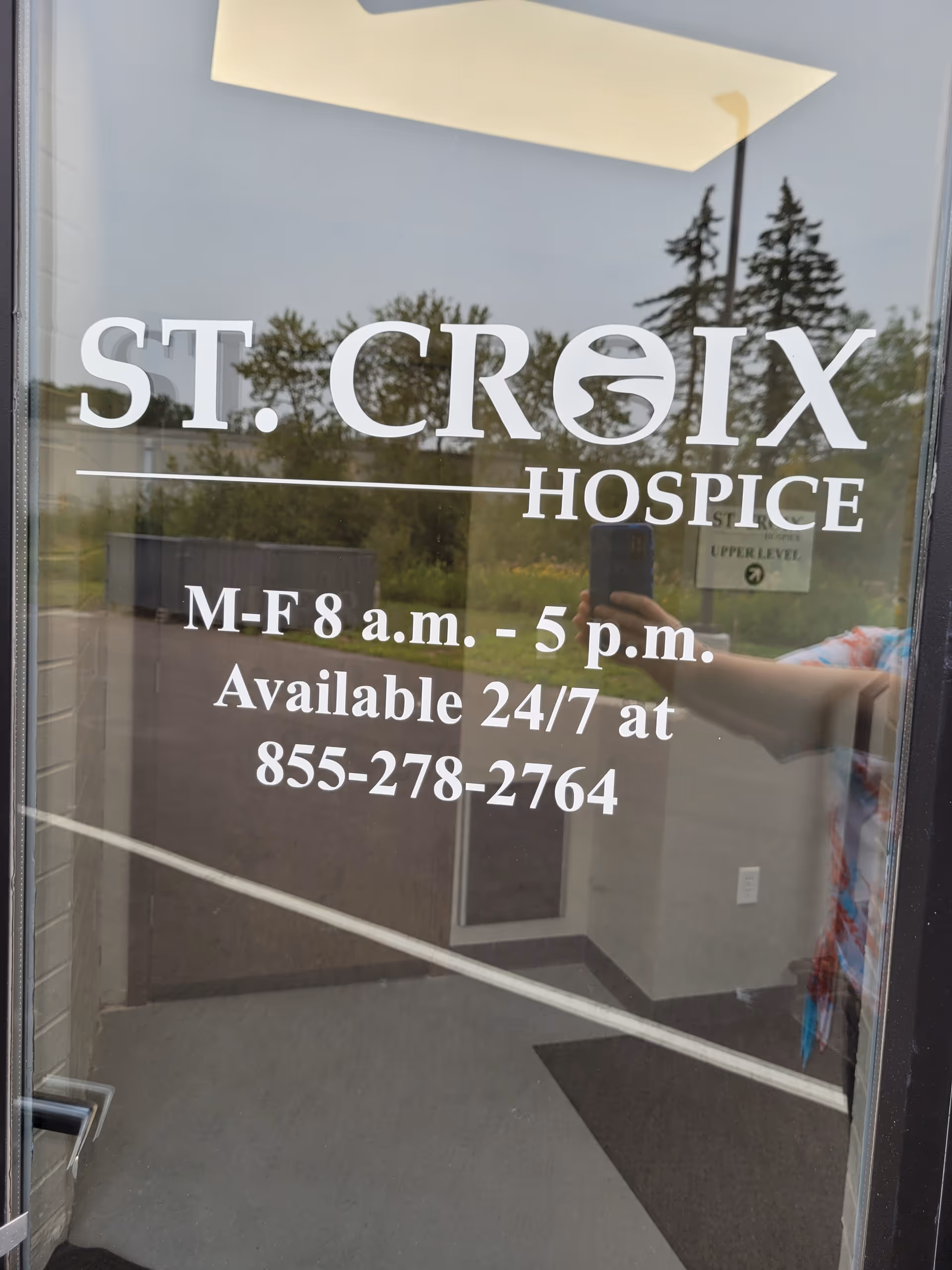 Glass door with St. Croix Hospice signage and reflection of trees outside.