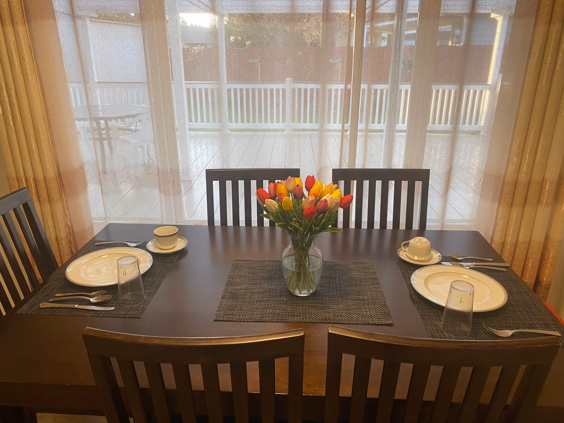 A dining table set for four with a vase of tulips near a bright window.