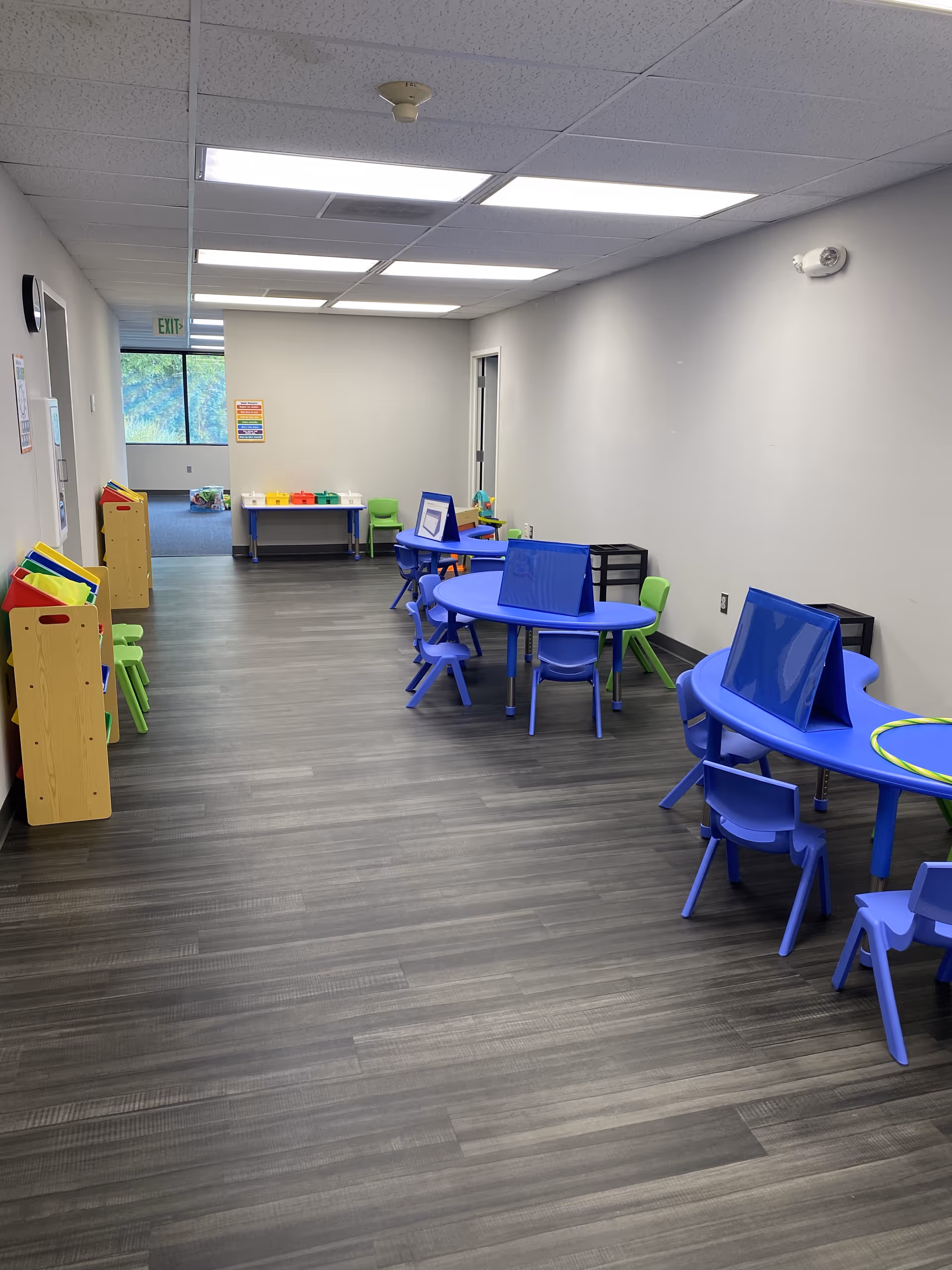 Bright activity room with blue tables, small chairs, and colorfully arranged toy stations.