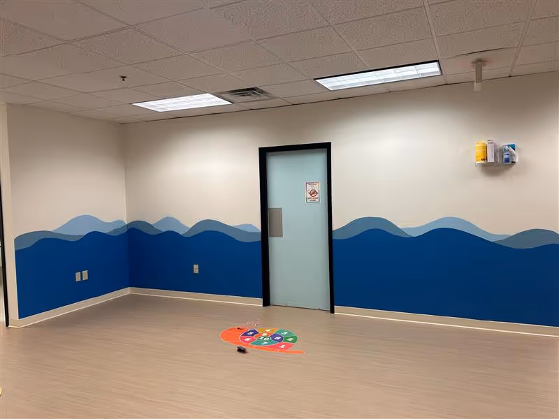 Interior room with blue wave mural on walls, doorway, and colorful floor markers.