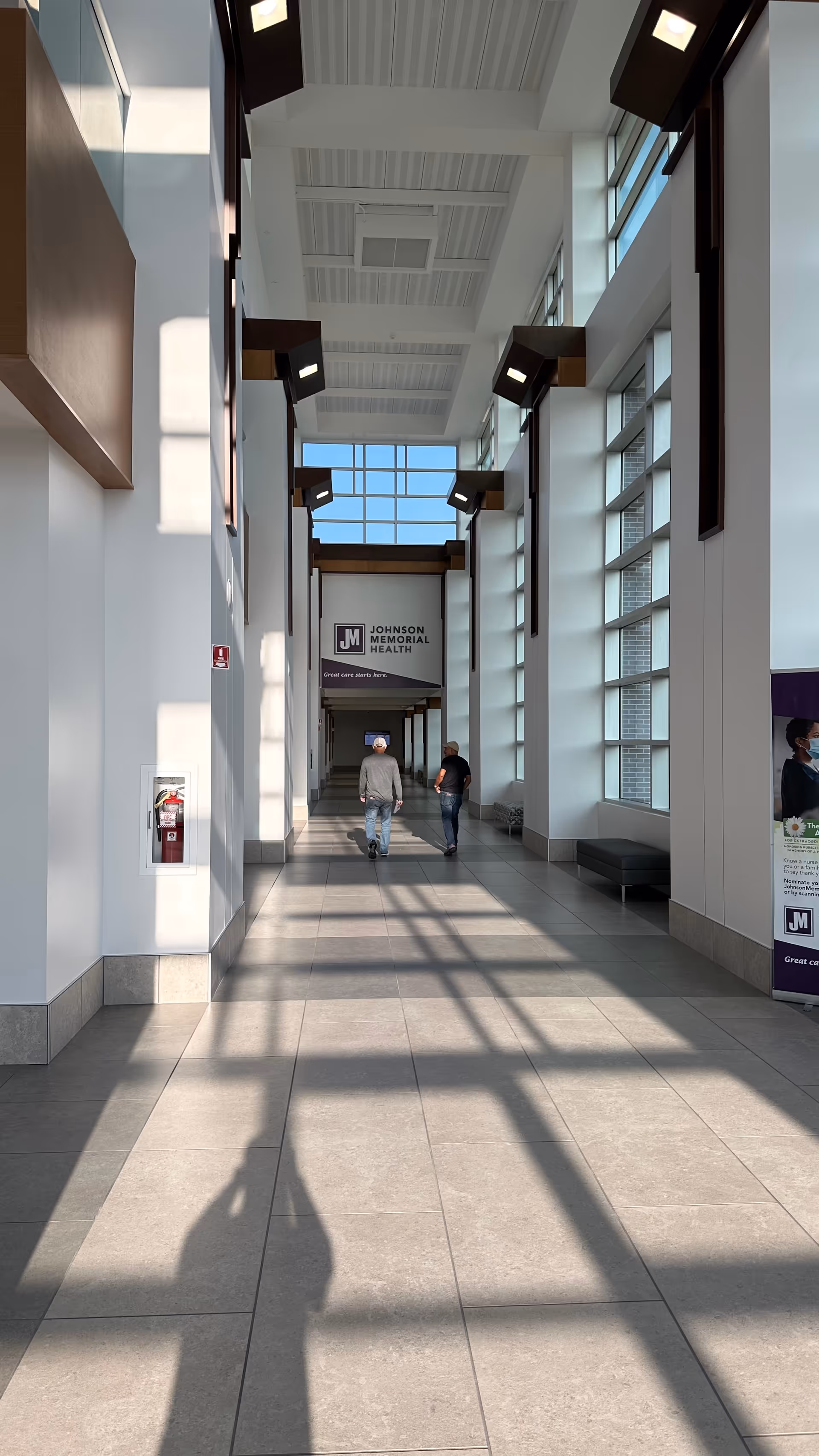 Bright interior corridor of a care facility with two people walking under Johnson Memorial Health sign.