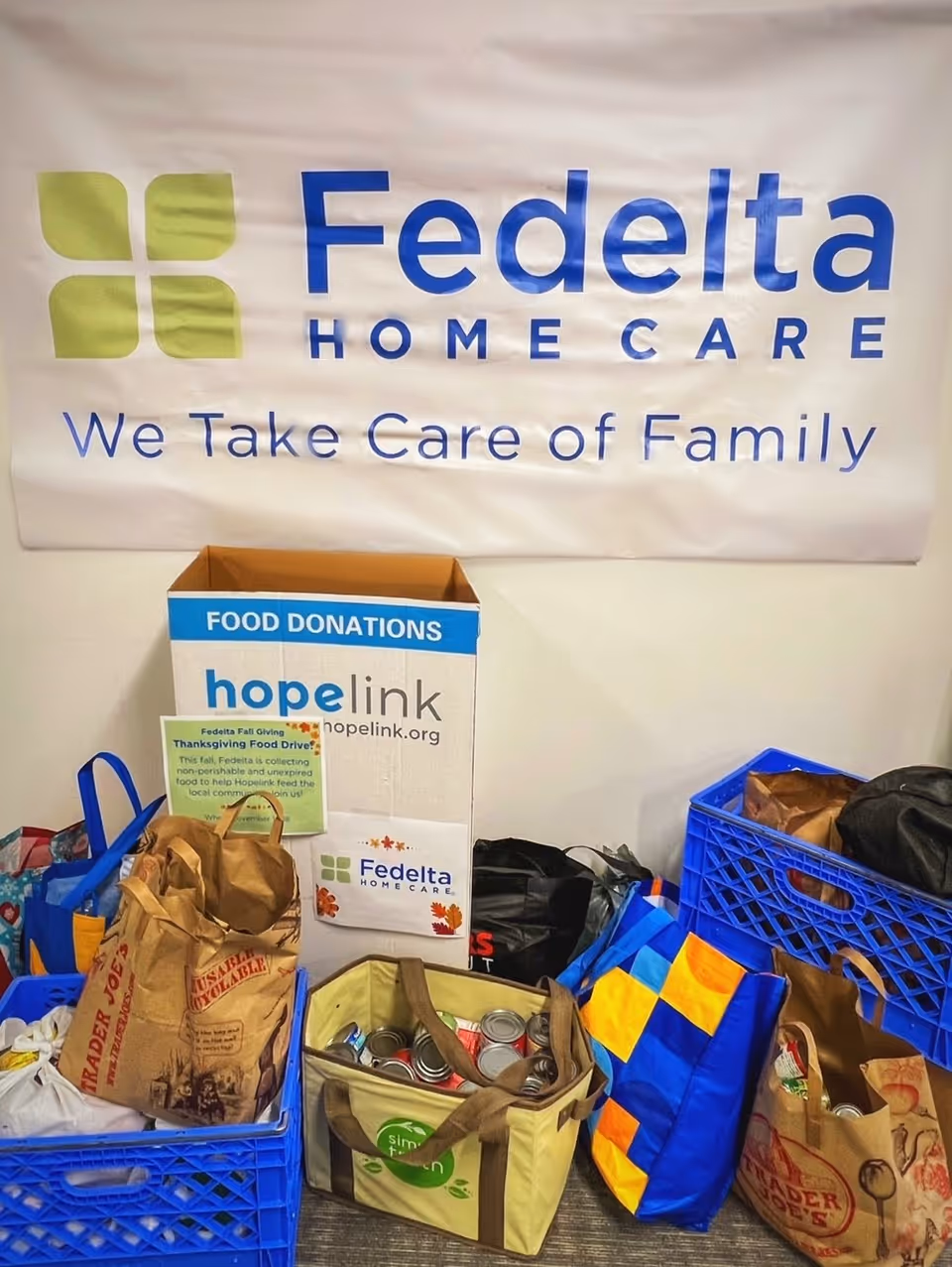 Fedelta Home Care banner with a food donations box and bags in an indoor lobby.