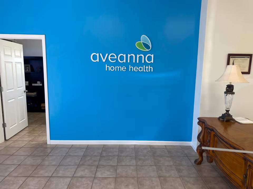 Bright blue wall with Aveanna Home Health logo, doorway, and wooden console table indoors.