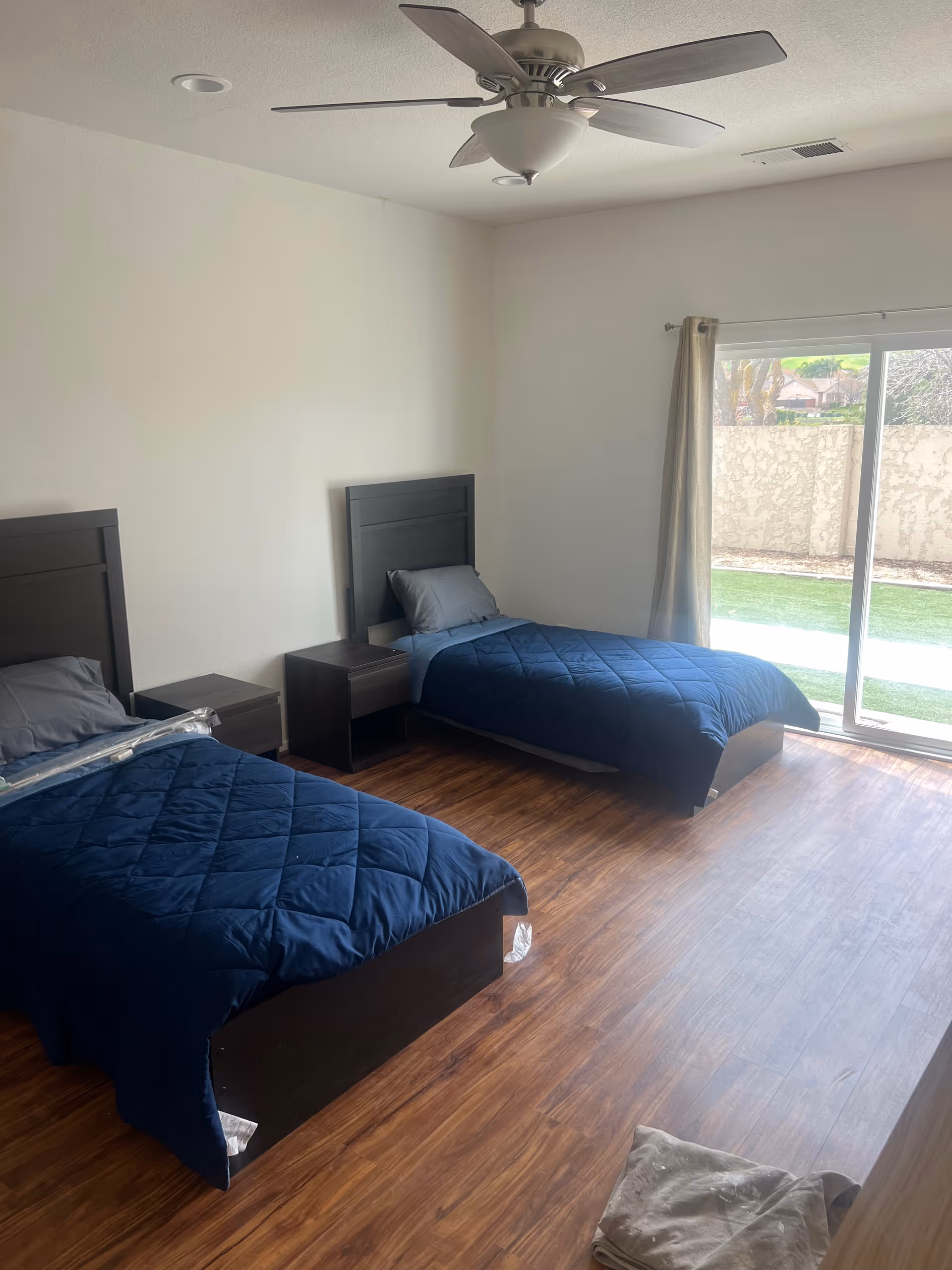 Two twin beds with navy quilts and nightstands in a bright bedroom with a sliding door.