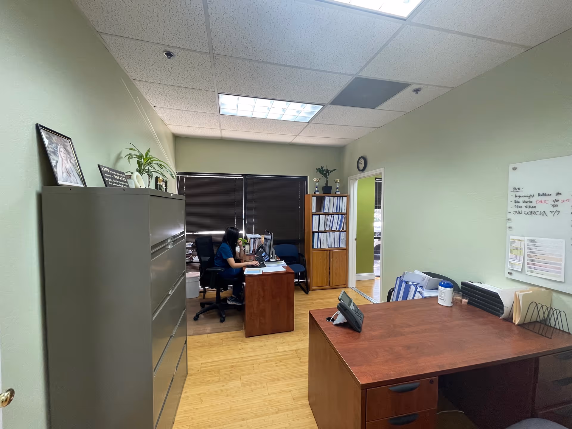Interior office with a staff member at a desk, filing cabinets, and shelves.
