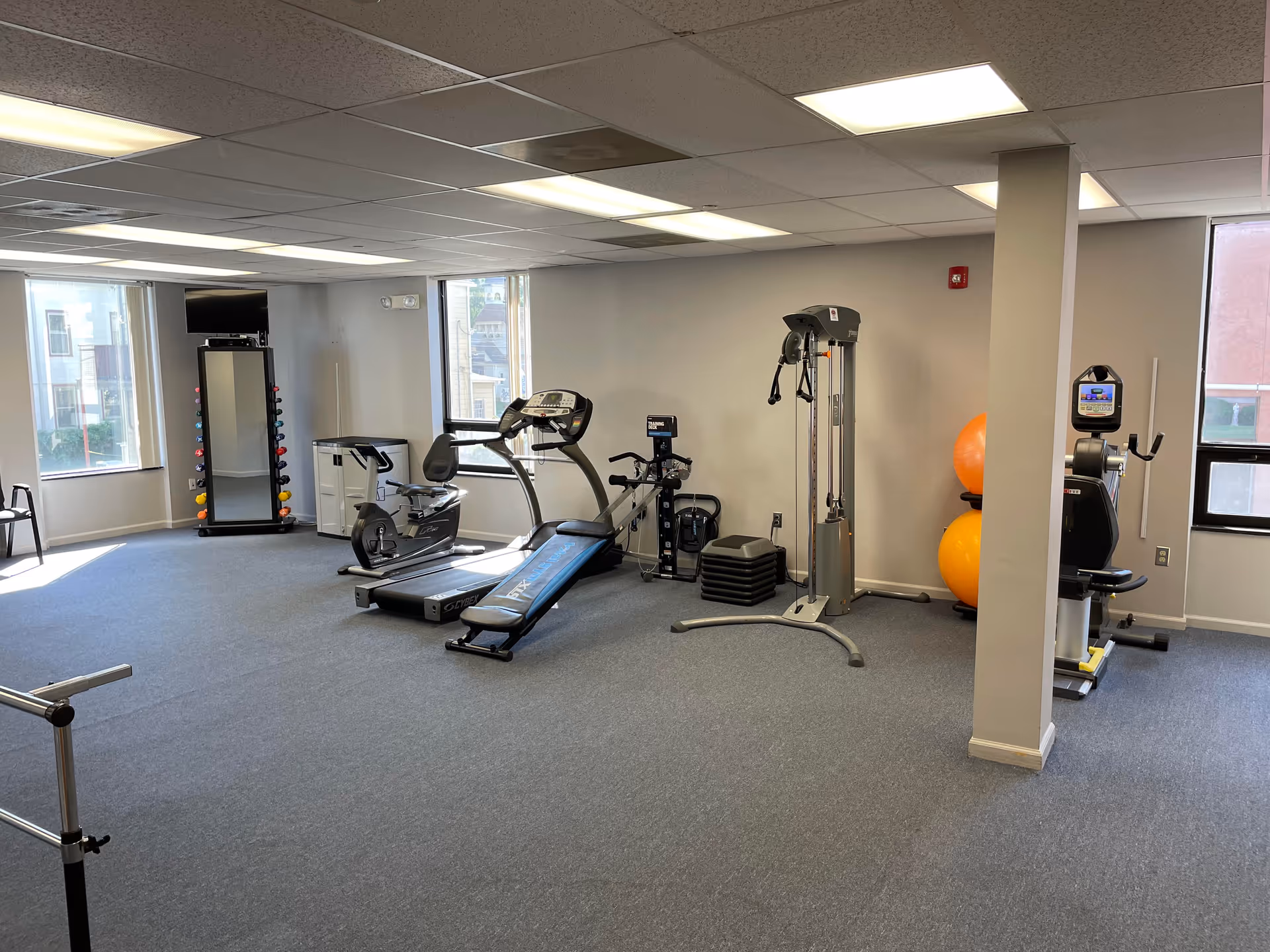 An interior fitness room with treadmills, weights, and exercise equipment in a senior living facility.