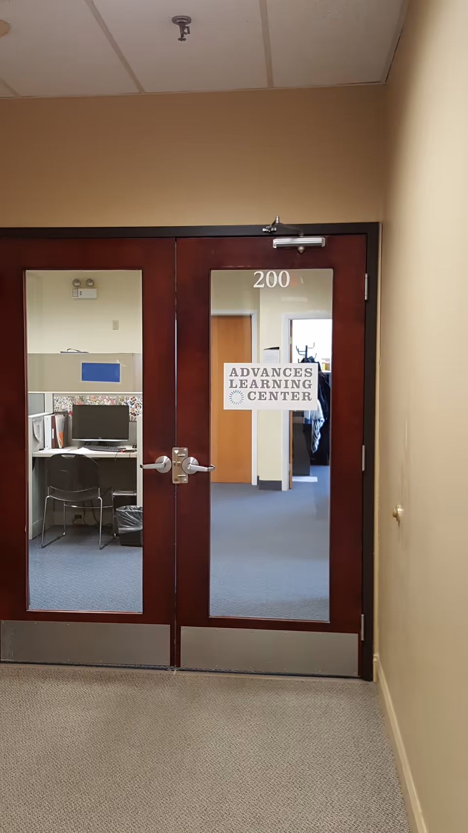 Doorway with glass doors labeled 200 opens to an office area and learning center sign.