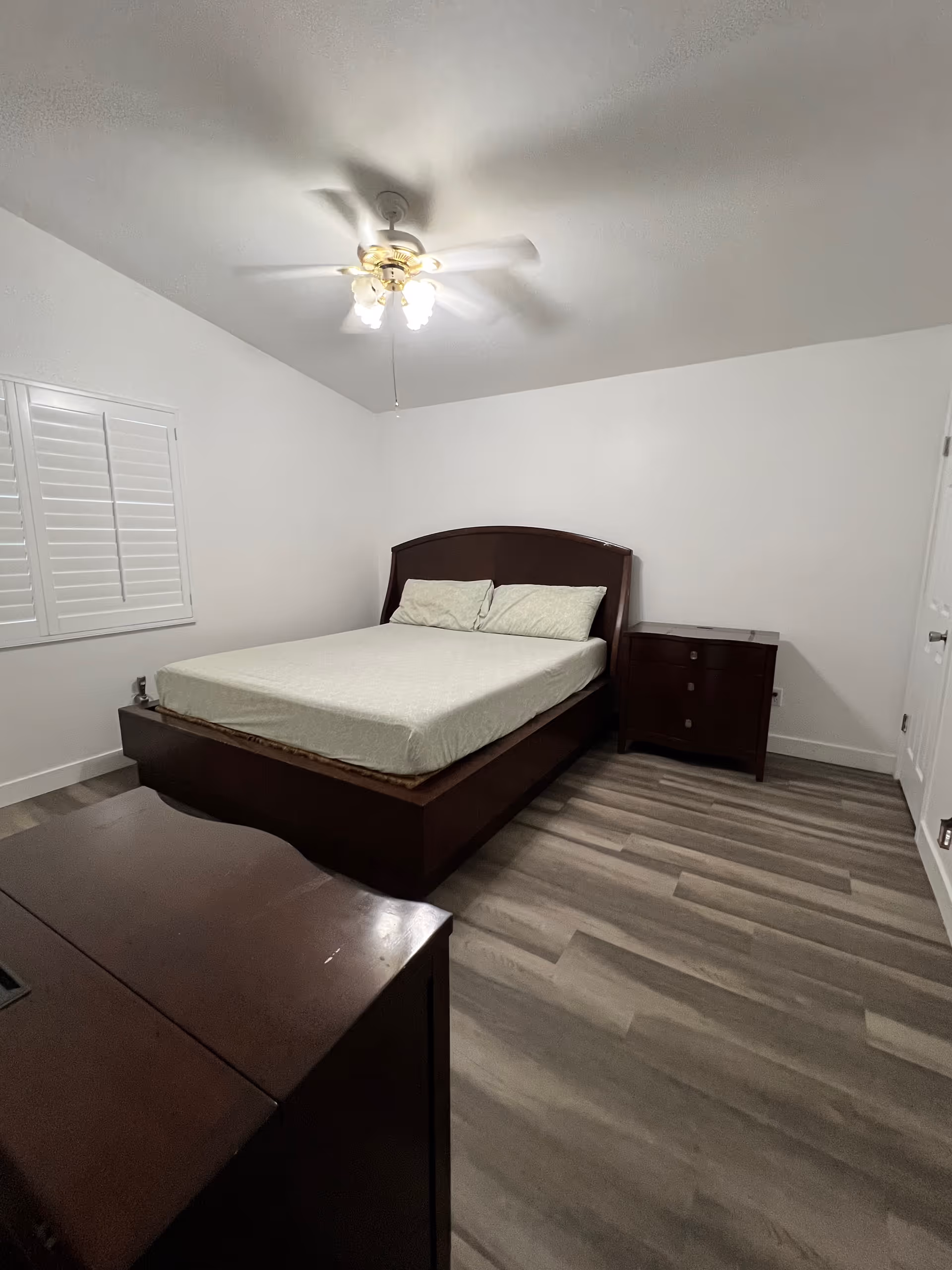 Dark wood bedroom with bed, nightstand, dresser, and ceiling fan.
