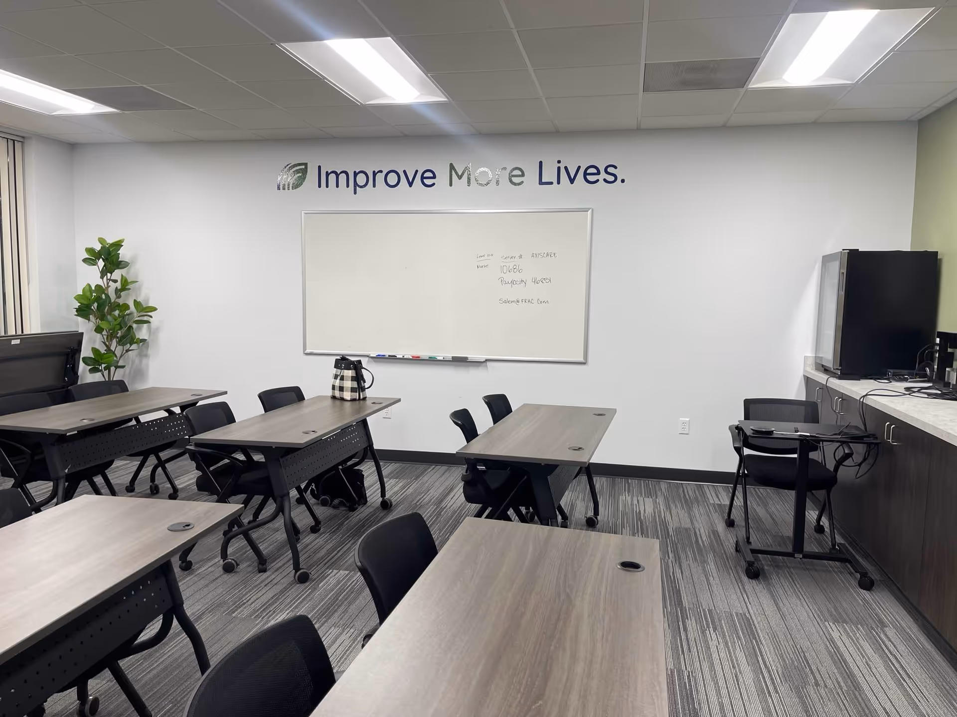 Classroom-style training room in a senior care facility with desks, chairs, whiteboard, and plant.