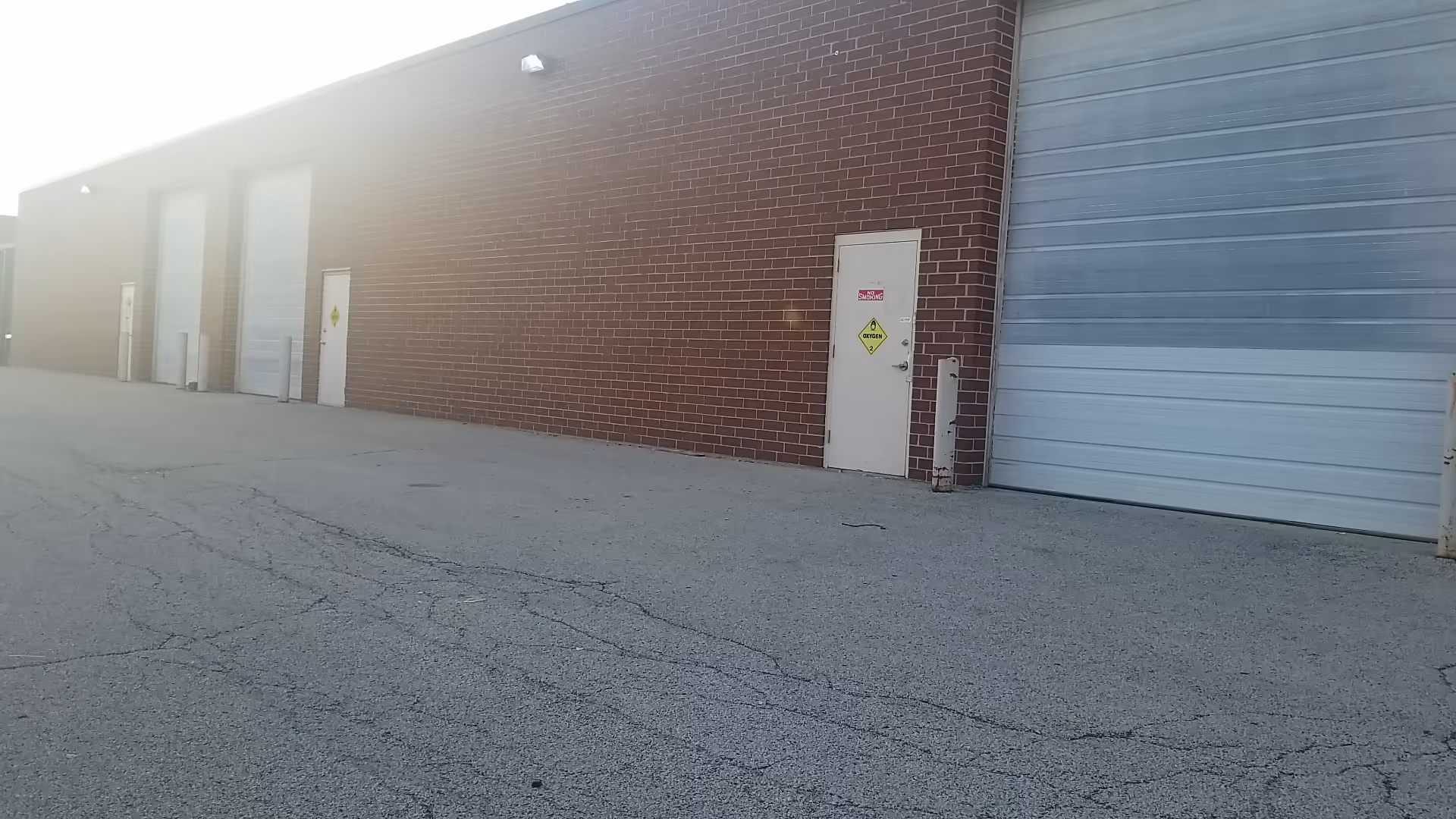 Exterior view of a brick facility with large metal loading doors and a small white door.