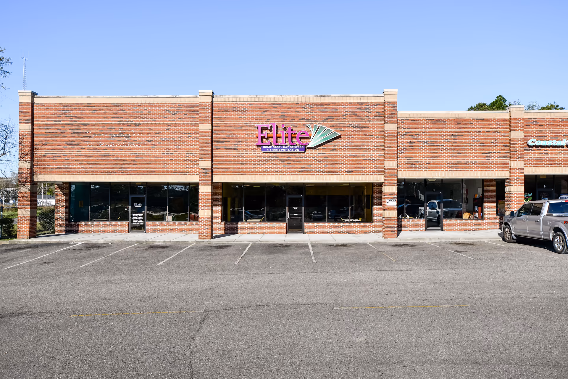 Brick storefront with Elite sign and large windows in a strip mall-style building.