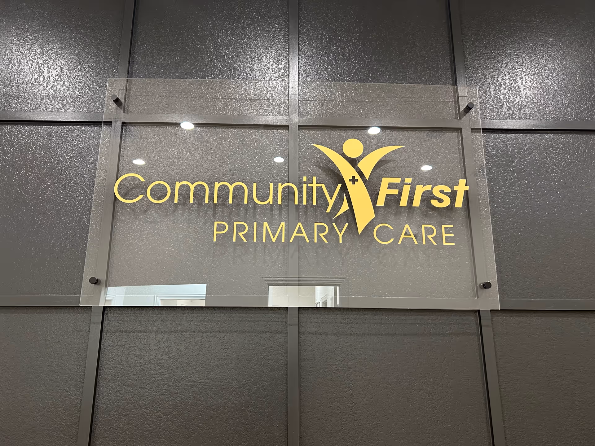 Acrylic sign reading Community First Primary Care mounted on a dark paneled interior wall.