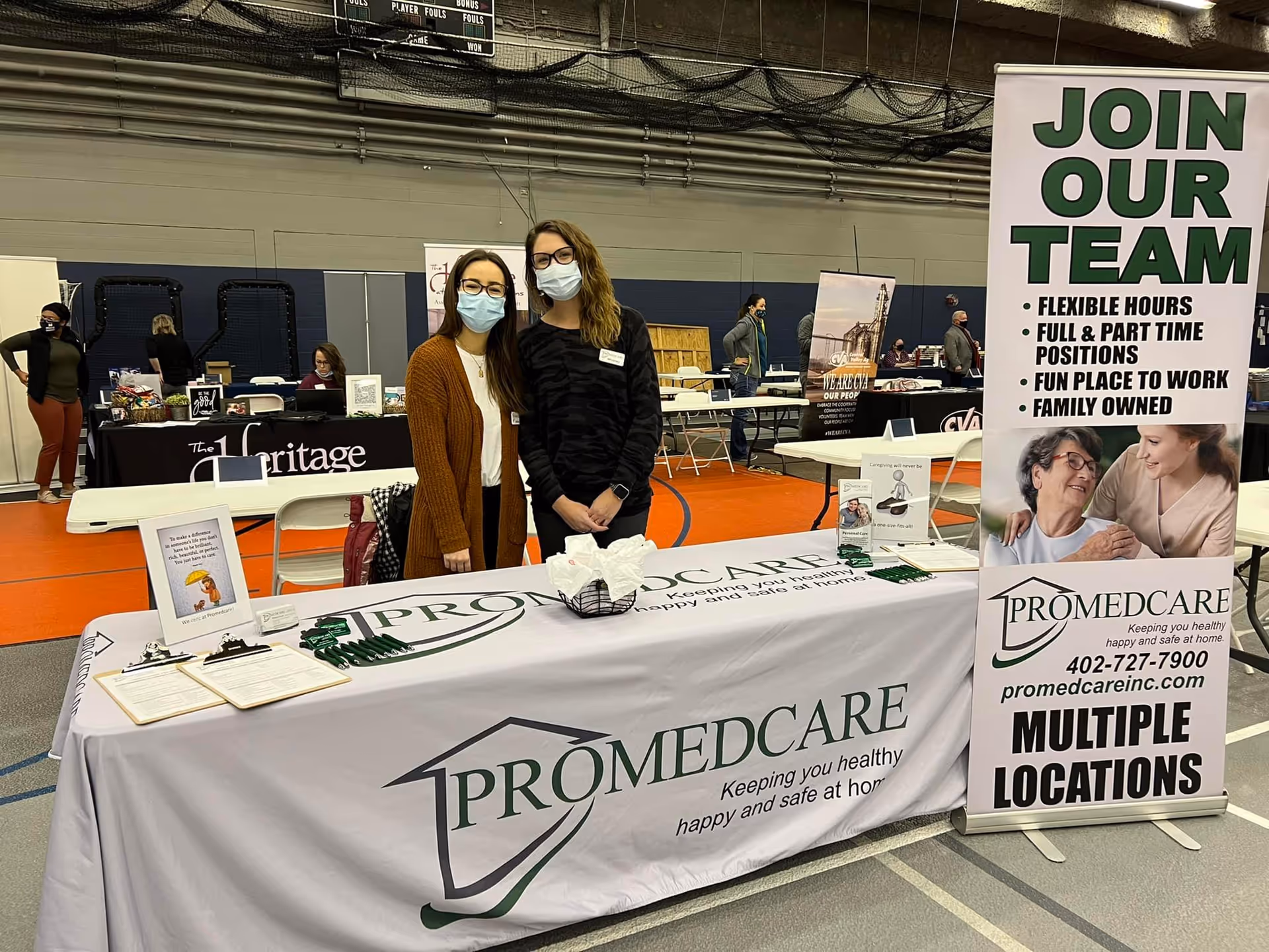 Two masked Promedcare staff members stand behind a booth at a community career fair.