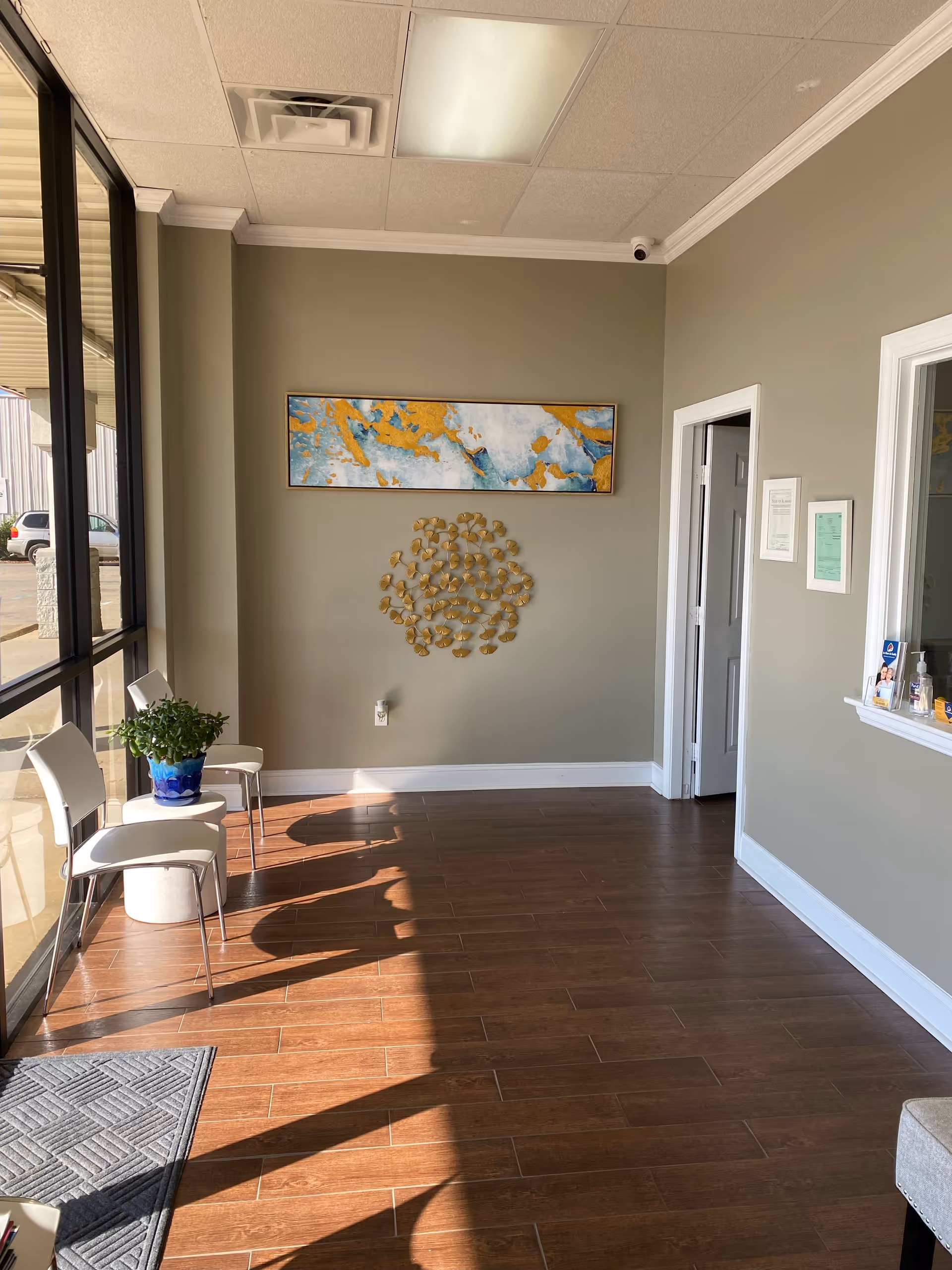 Sunlit lobby area with chairs, potted plant, wall art, and decorative metal sculpture.
