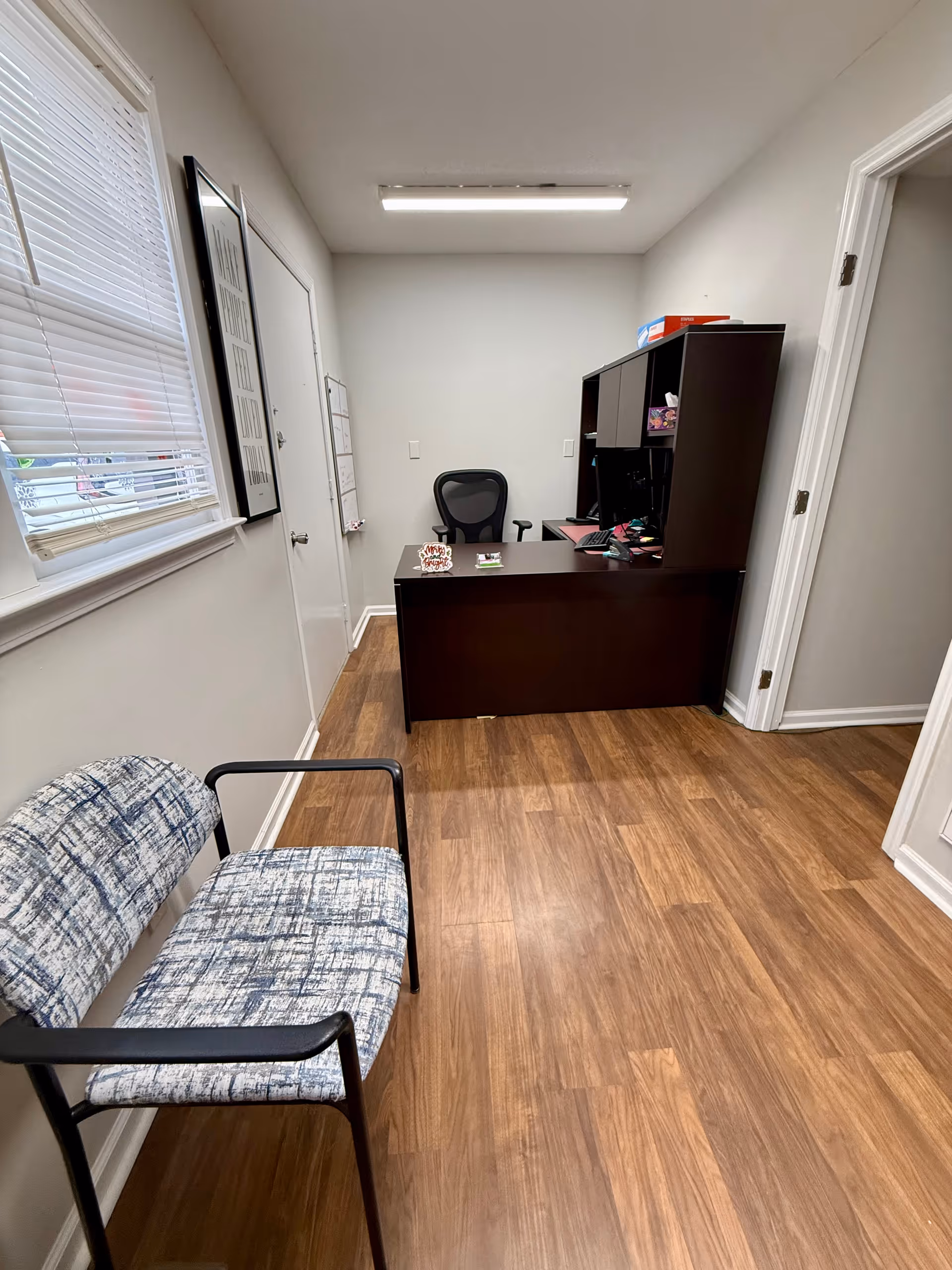 Reception desk with chair, bookshelf, and waiting chair in an office hallway.