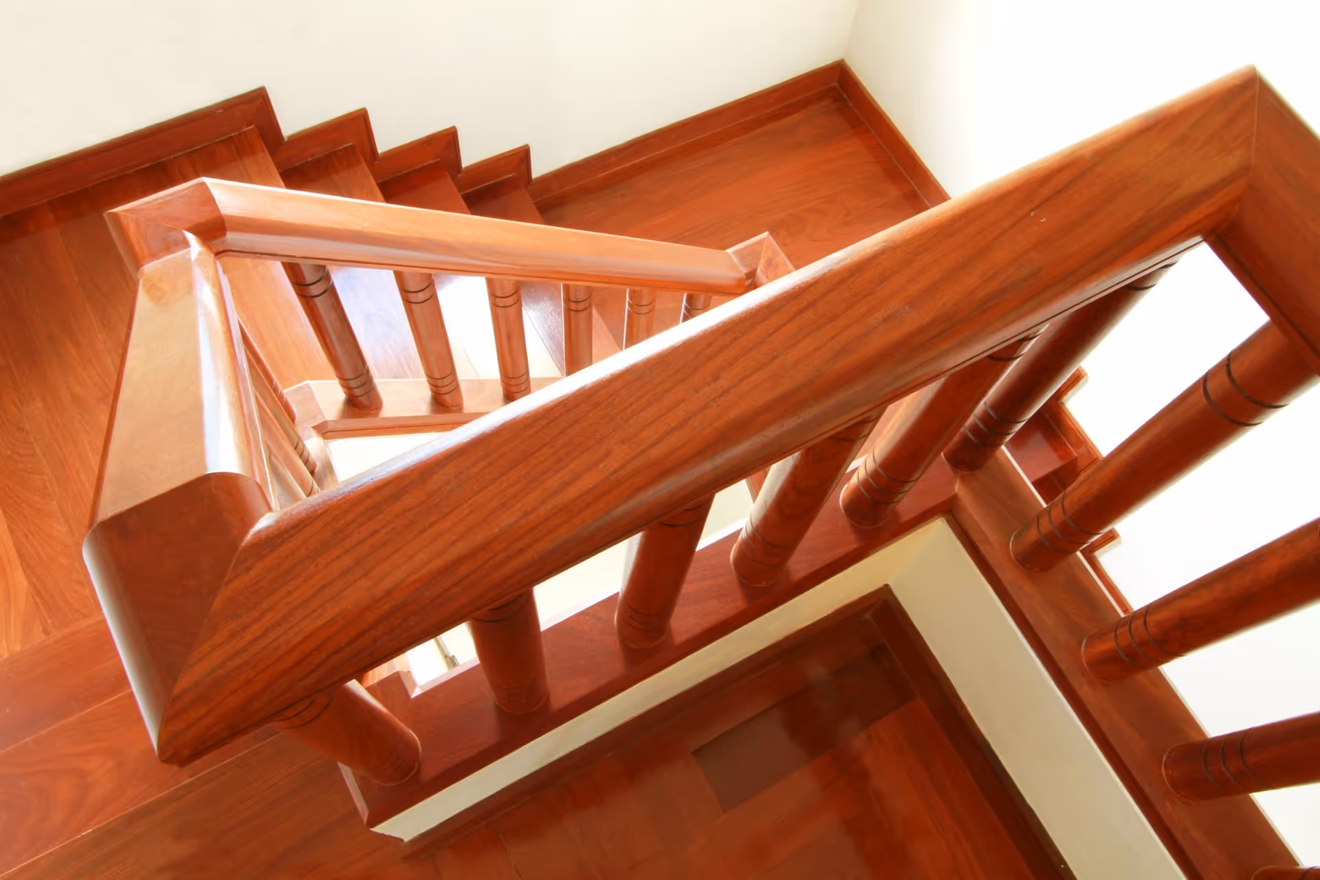 Overhead view of a polished wooden staircase with railing balusters in an interior hallway.