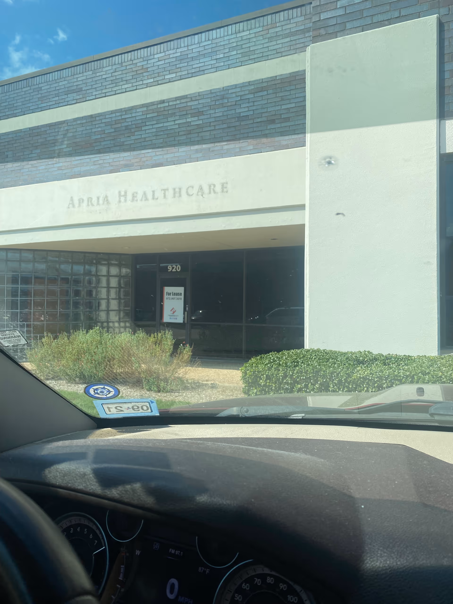 Exterior view of Apria Healthcare building entrance with shrubs and a parked car.