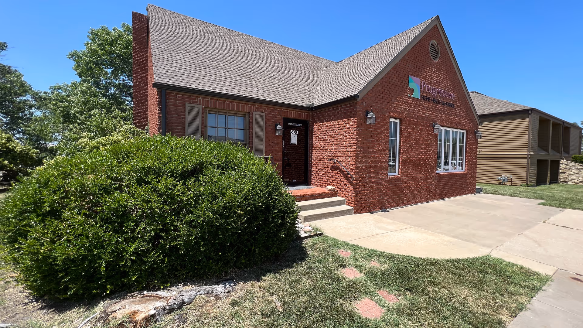 Brick building labeled Progressive Home Health & Hospice with front entrance, steps, and driveway.